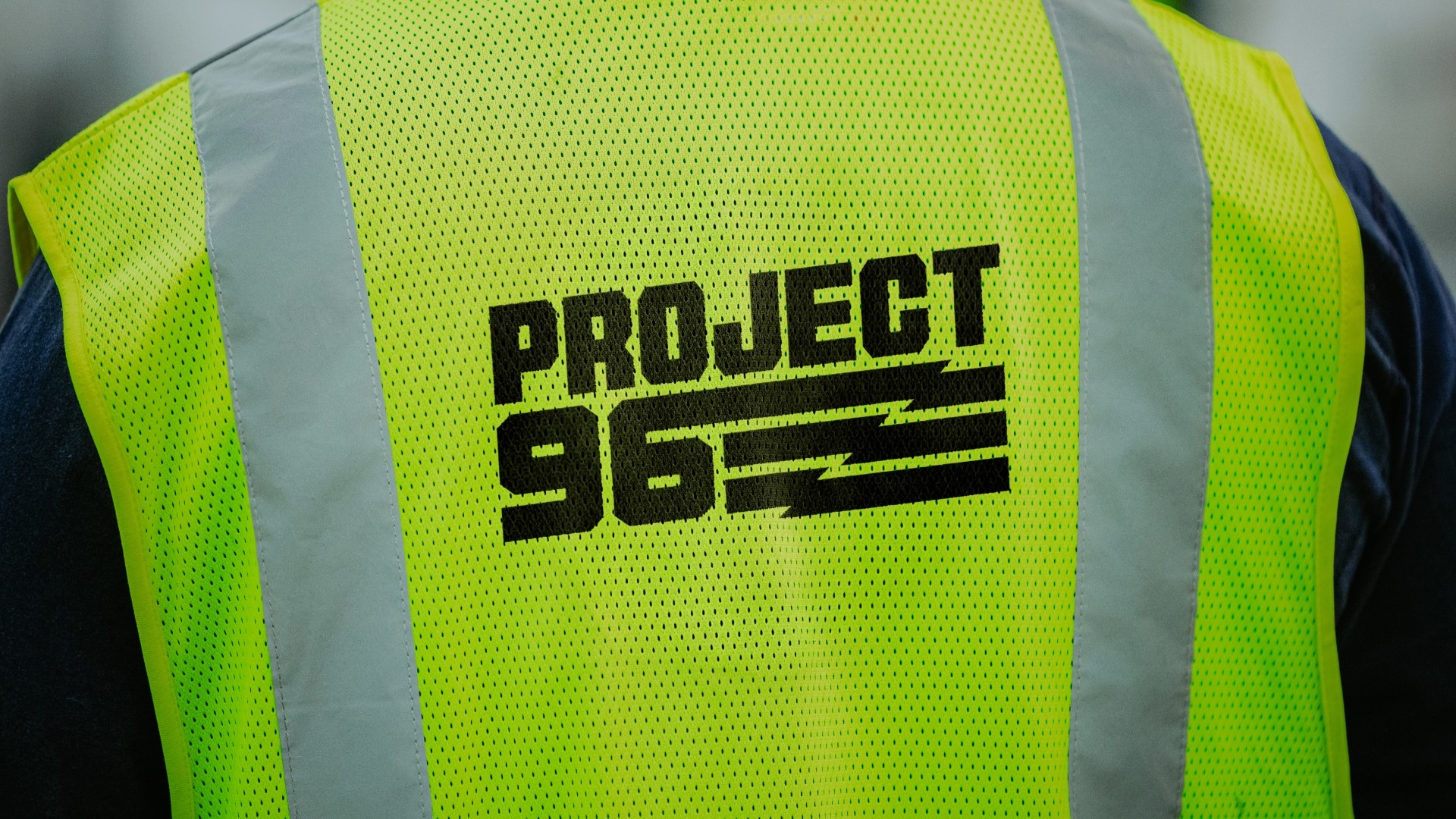 Close-up of a high-visibility yellow safety vest with black text reading 'PROJECT 96' and horizontal lines.