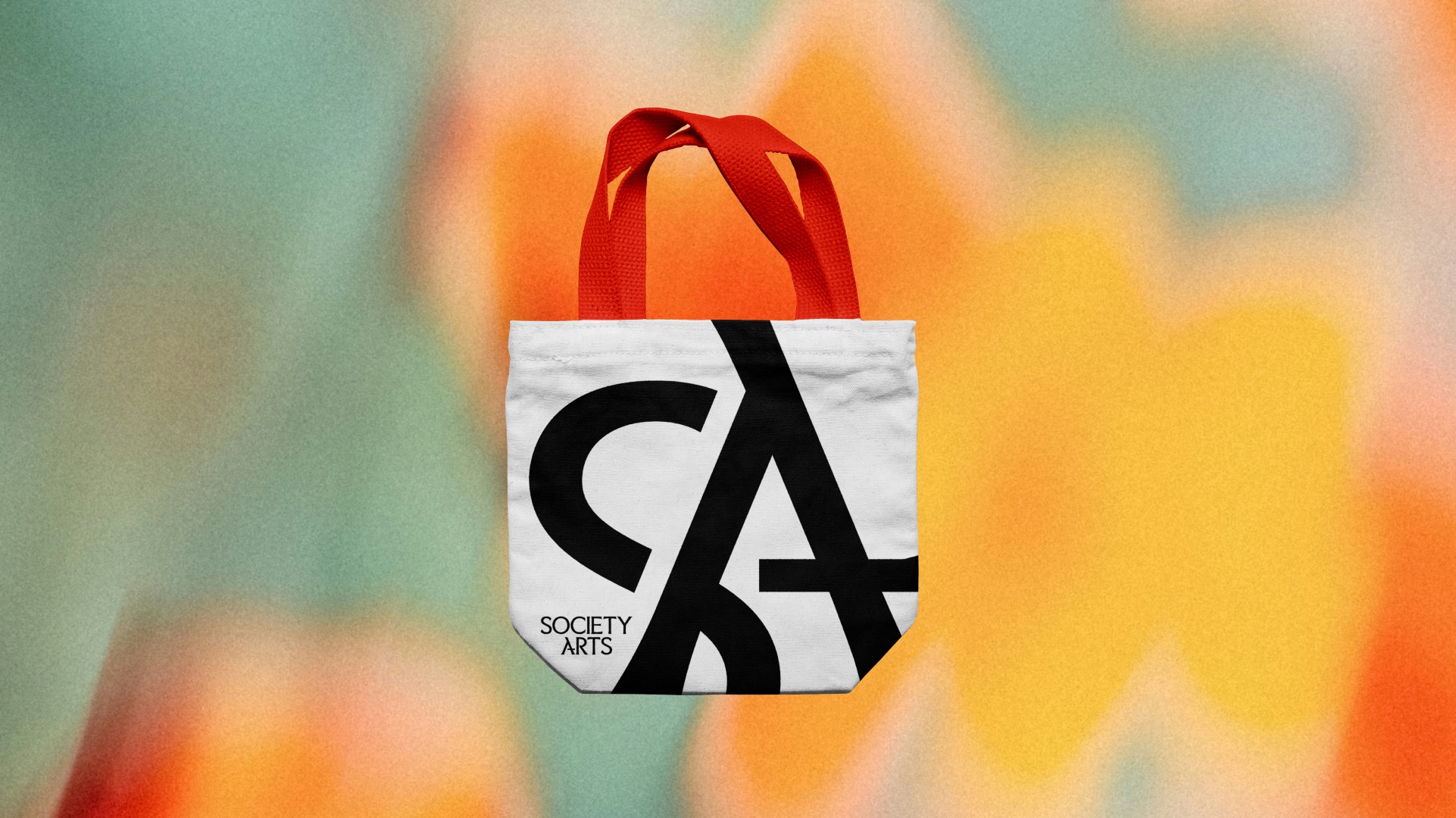 Small tote bag with red handles and black and white design, against a colorful blurred background.