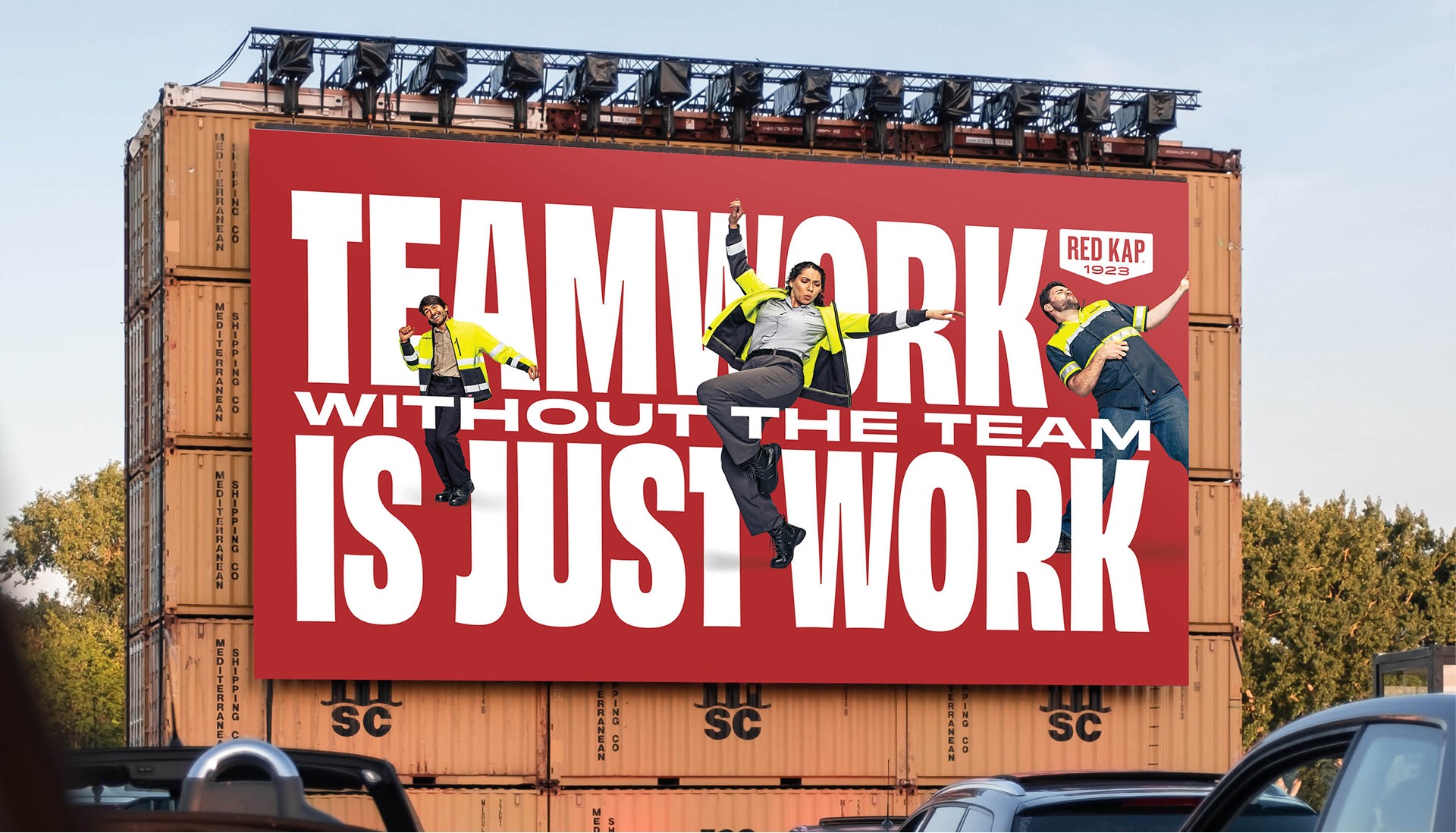 Two construction workers in safety gear on a large billboard with a motivational message about teamwork and work.