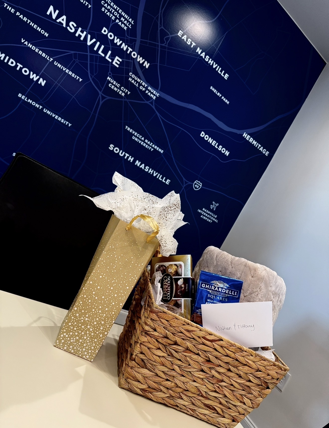 Gift box, basket with items, and a white envelope on a table in front of a blue map background.