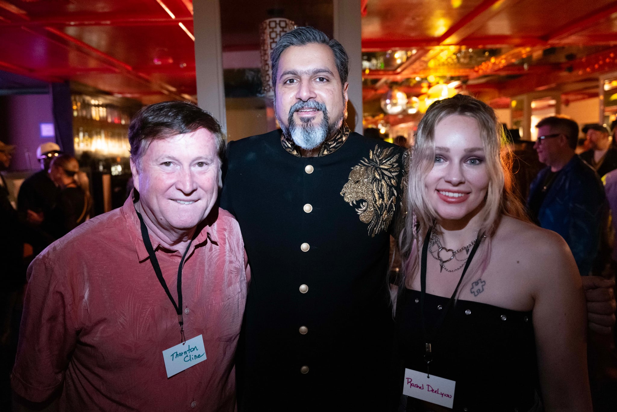 Three people smiling at a social event, two women and one man, in a decorated indoor setting.