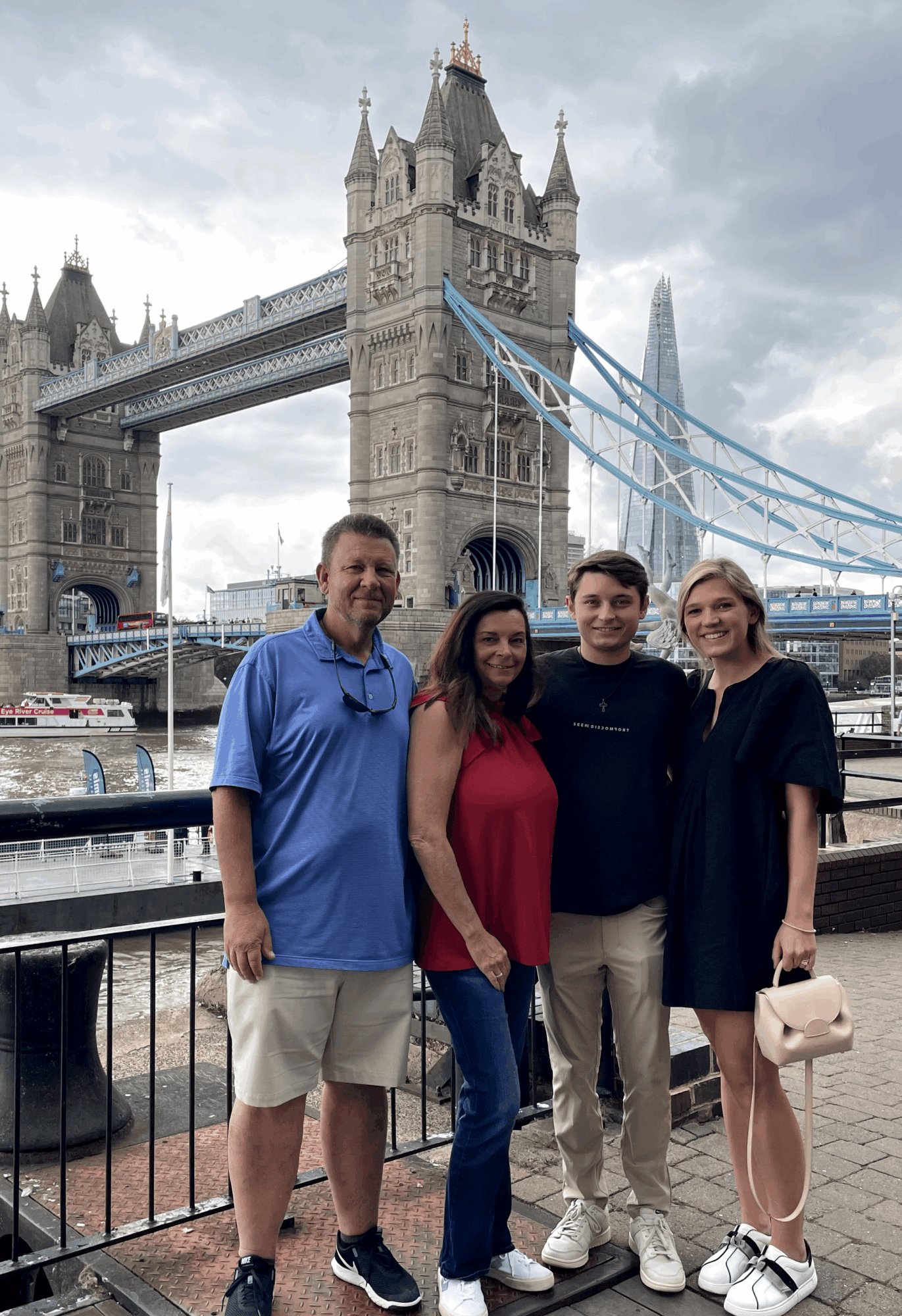 Four people stand in front of Tower Bridge in London, with the bridge and river in the background.