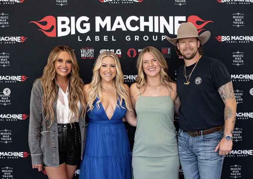 Four people standing in front of a backdrop with 'Big Machine' logo, smiling, posing for a photo.
