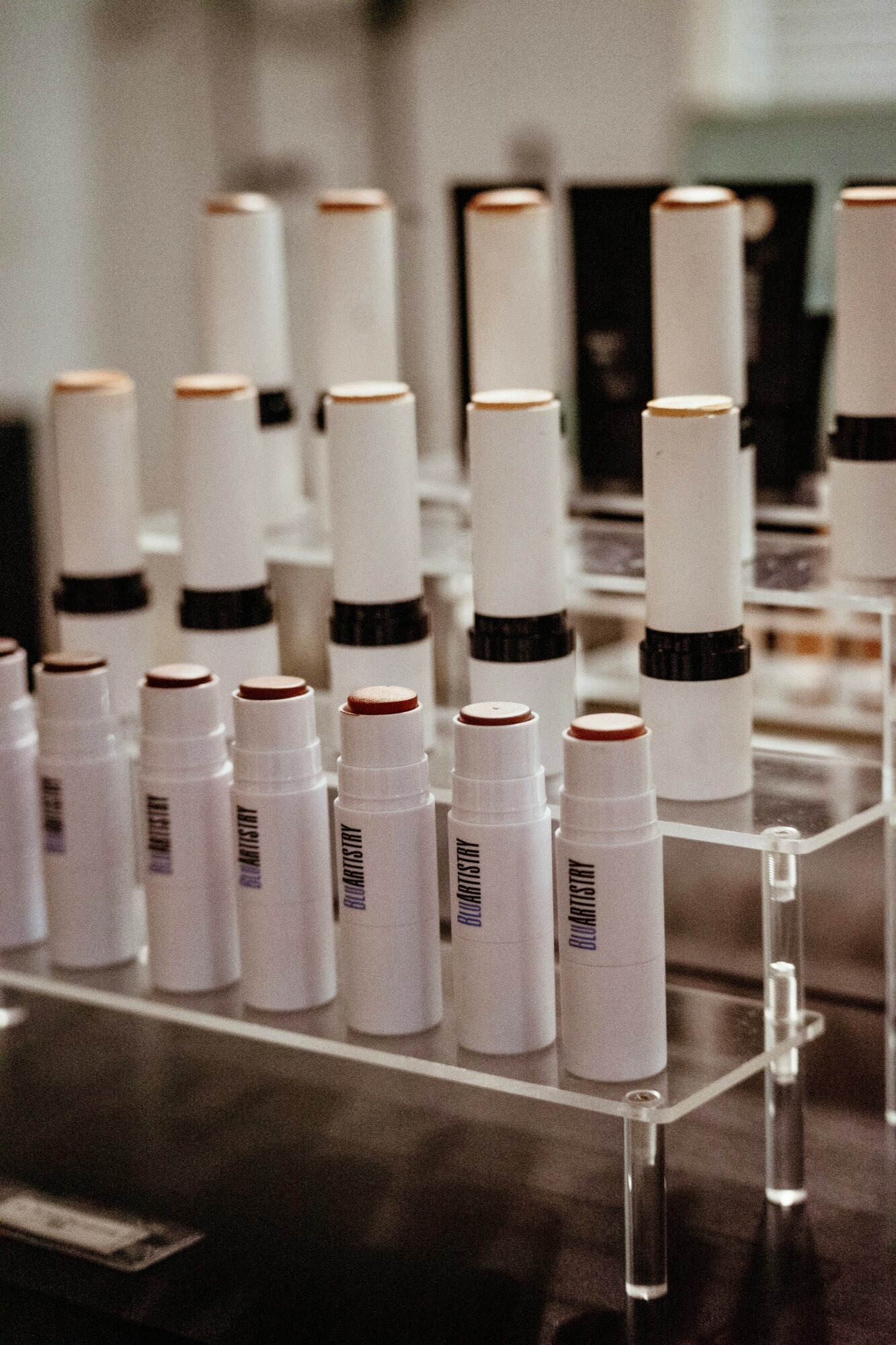 Multiple white cylindrical bottles with black bands arranged on a transparent display stand, some with red markings, in a retail setting.