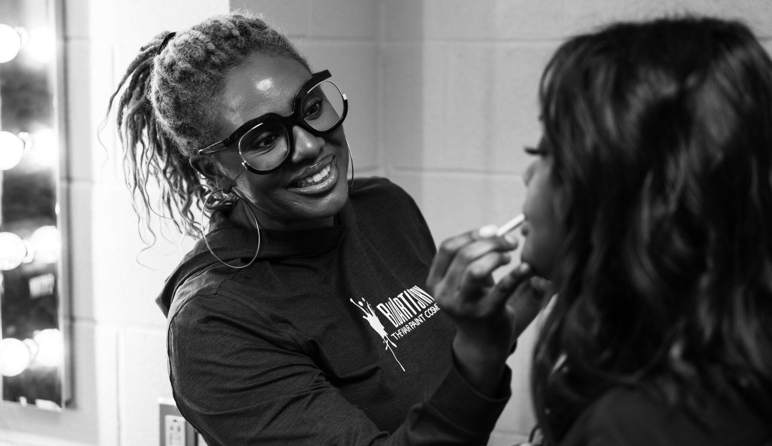 Makeup artist applying makeup to a person's face, smiling, in a professional setting.