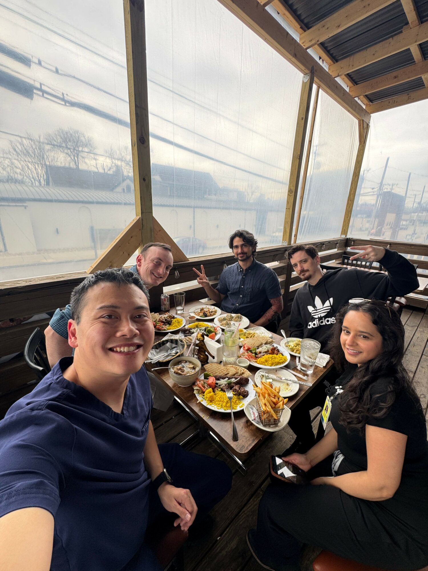 Group of people sitting at a table with food, in a room with large windows and wooden beams, smiling and looking at the camera.