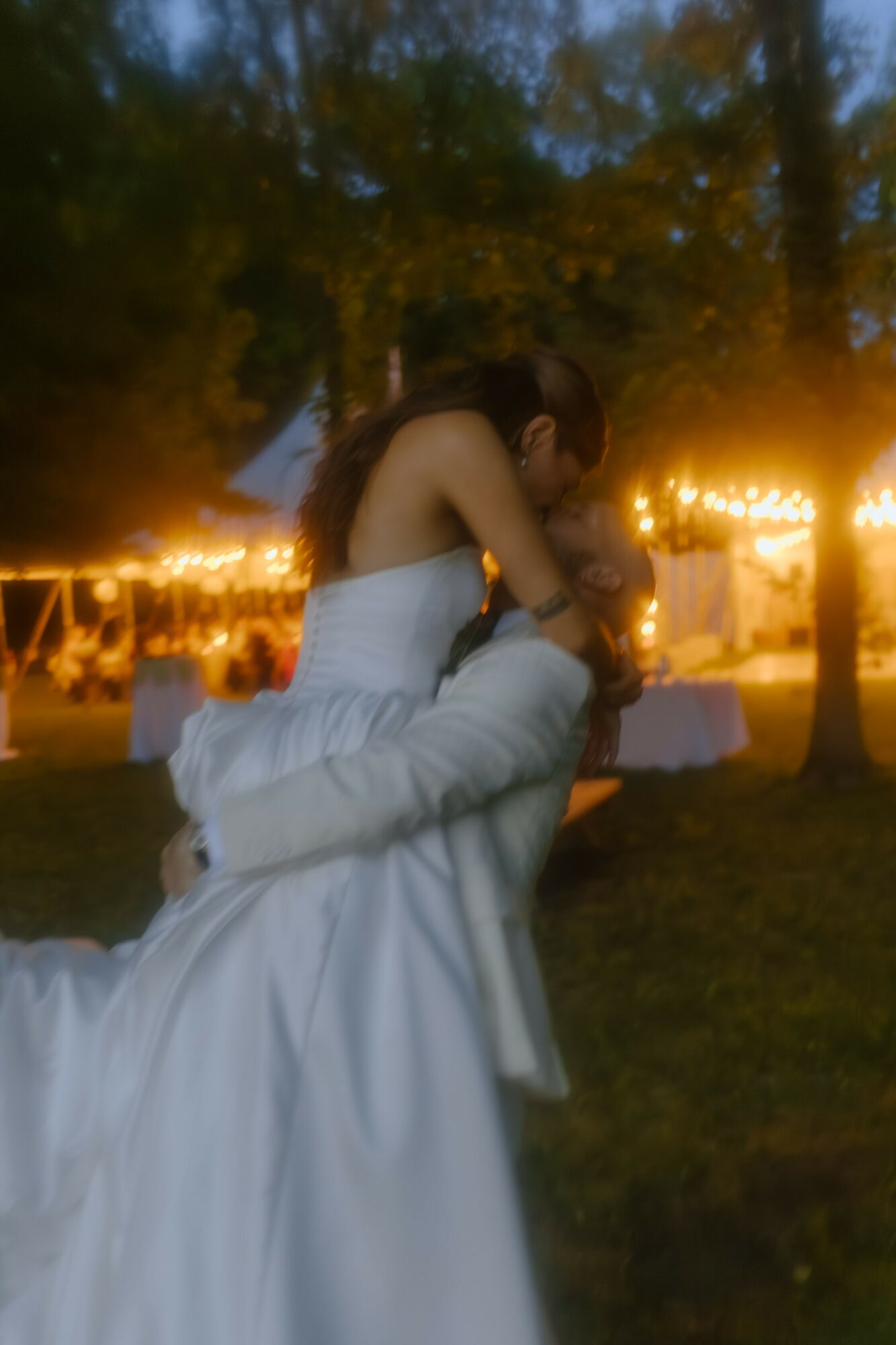 Person in a white dress being lifted outdoors at night with string lights and trees in background.