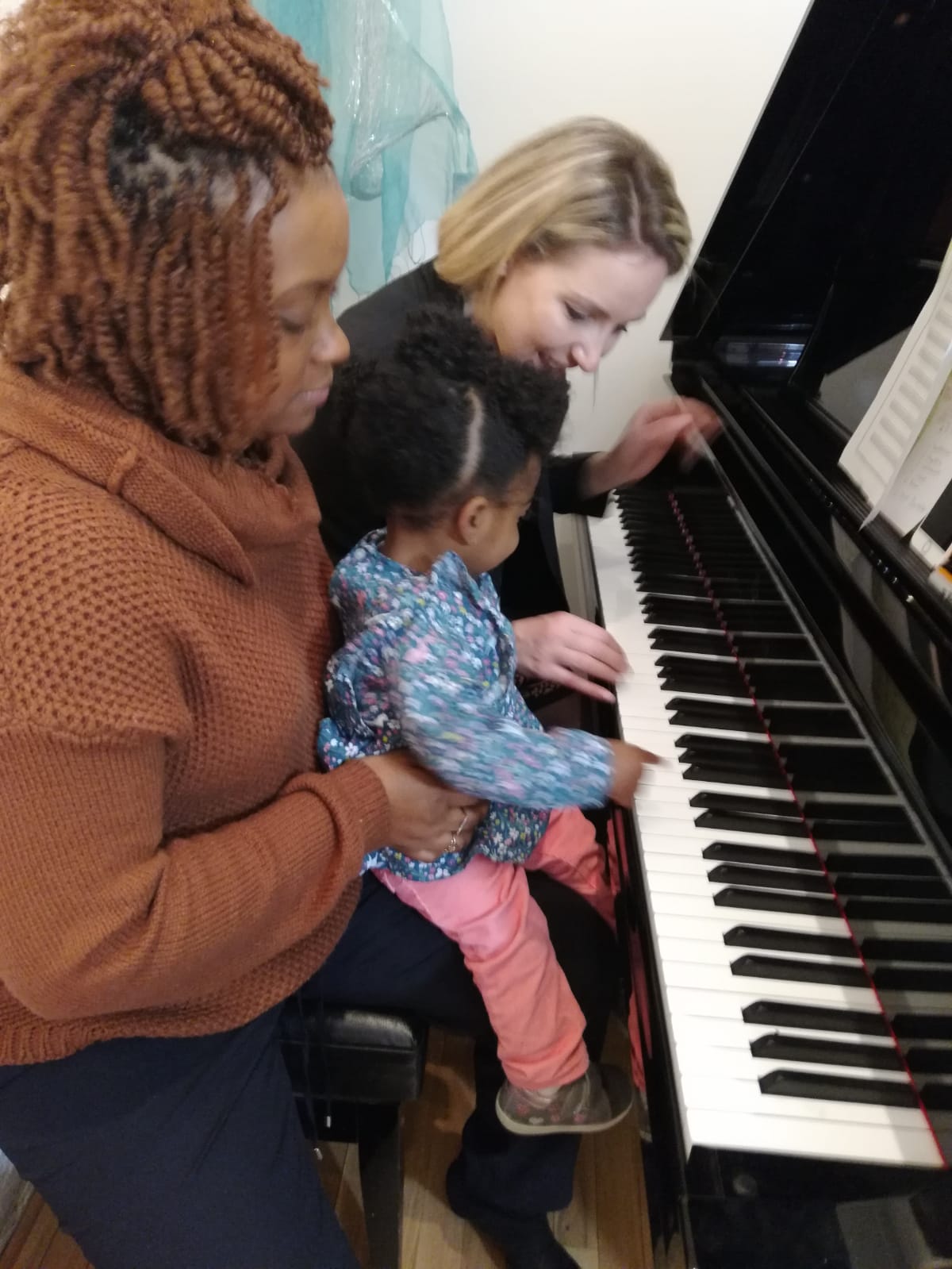 Three people, including a child, sit at a piano, looking at sheet music and playing together.