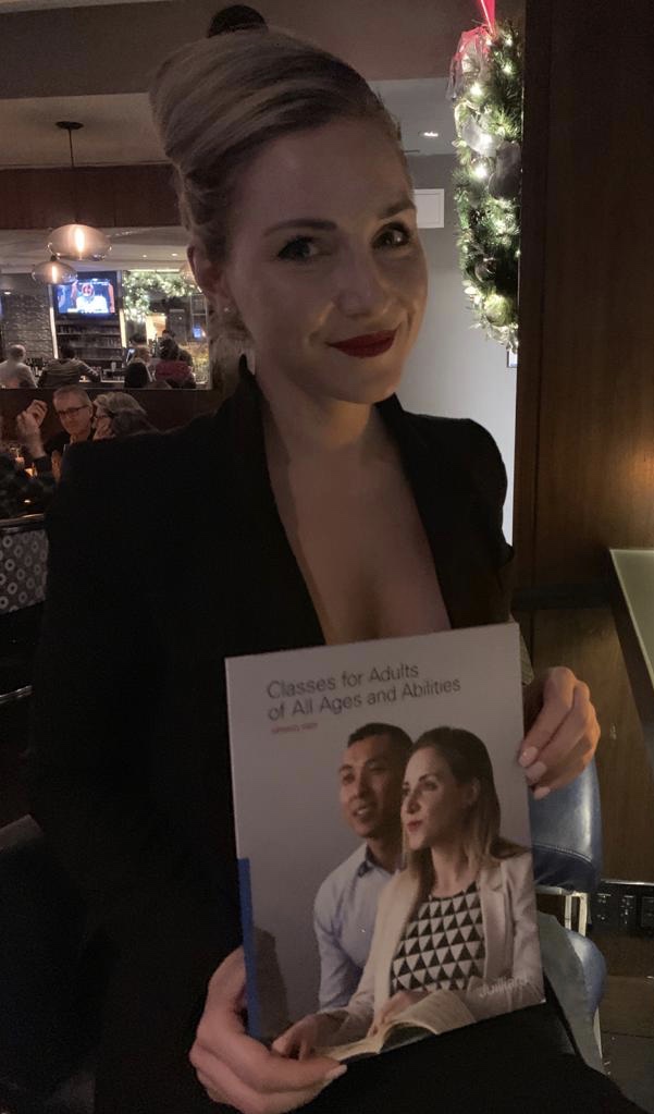 Woman with styled hair and red lipstick holding a magazine in a dimly lit festive setting.