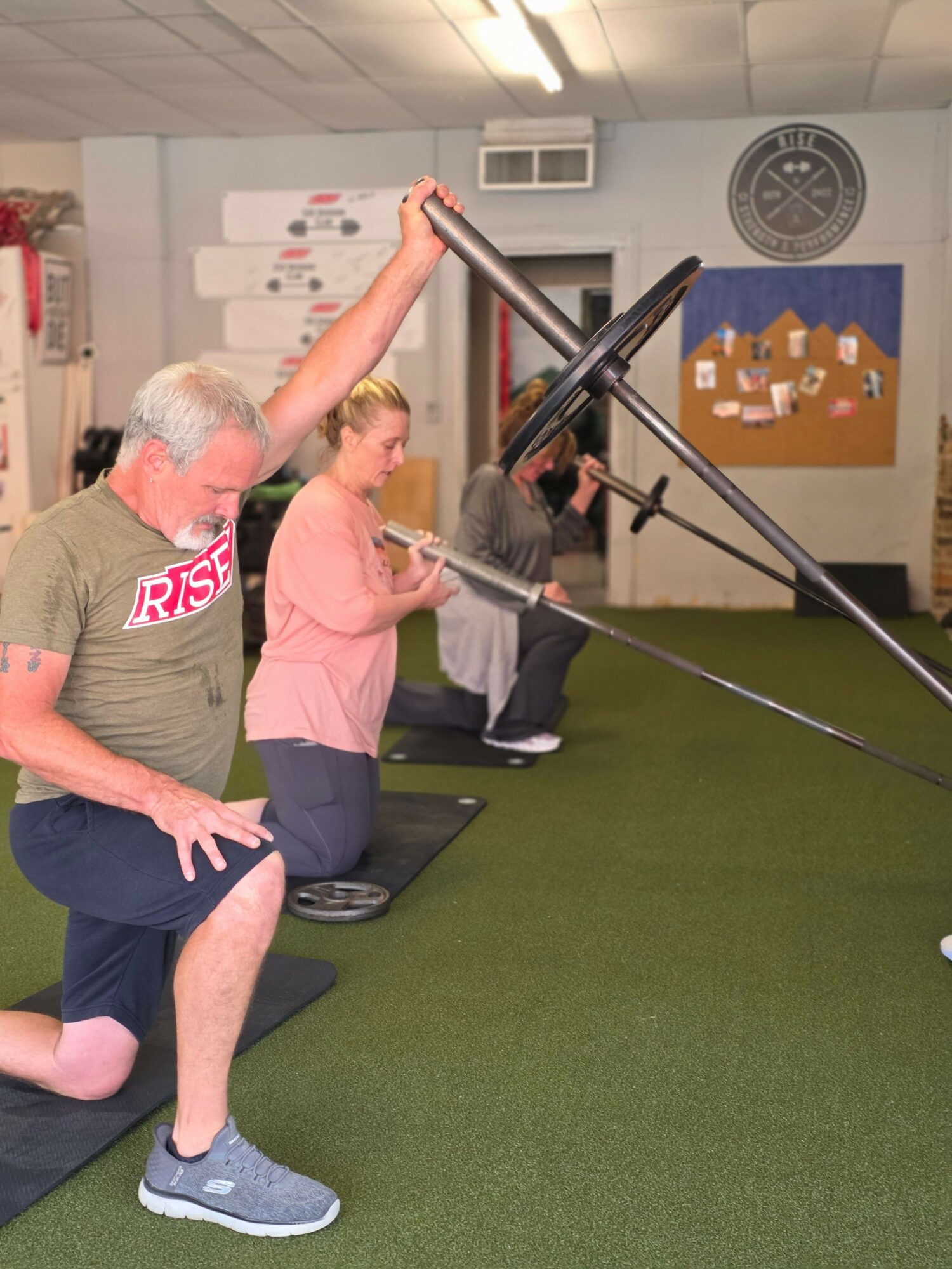 Person with gray hair and glasses pushes a person in a pink shirt on a swing indoors, with a green carpeted floor.