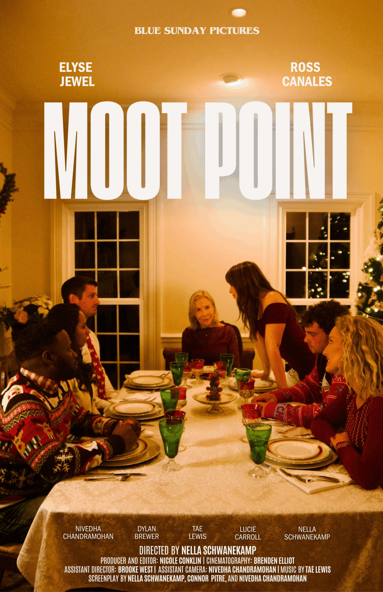 People sitting around a dining table with plates and glasses, a woman standing, in a warmly lit room with windows and a Christmas tree.