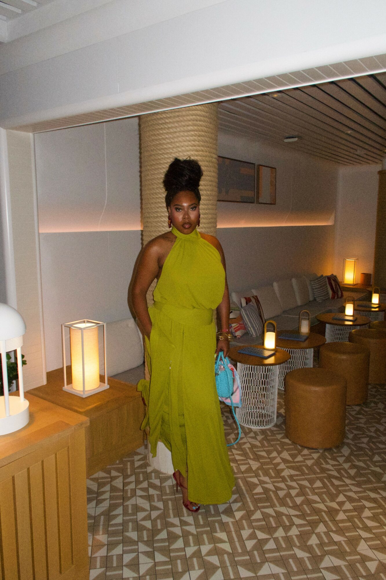 Woman in a bright yellow dress standing in a hotel room with modern decor, patterned carpet, and warm lighting.