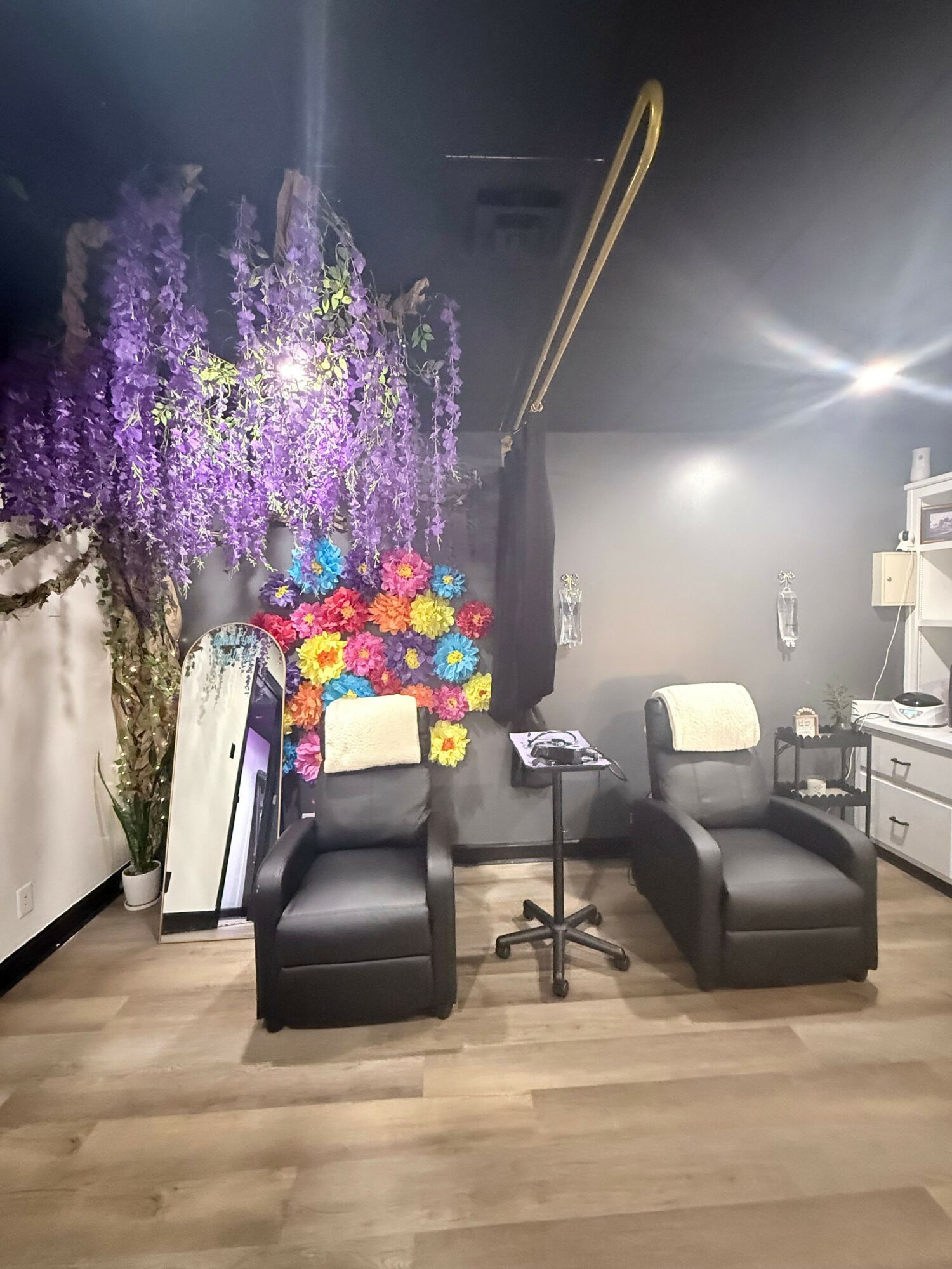 Indoor space with black chairs, a white cushion, colorful flowers, and purple flowering plant against a dark wall.