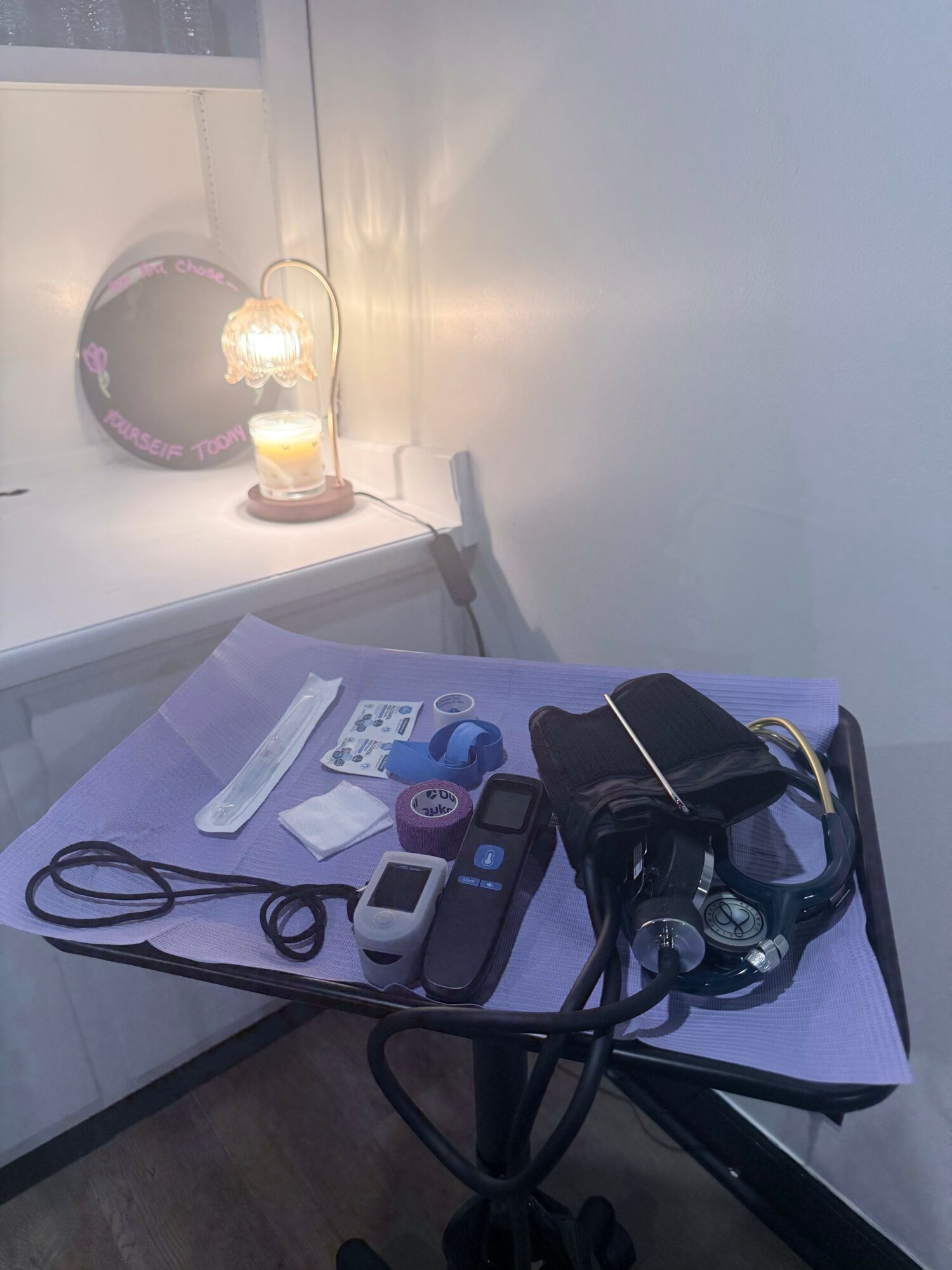 A table with electronic devices, cords, and papers next to a wall with a mirror and a light fixture.