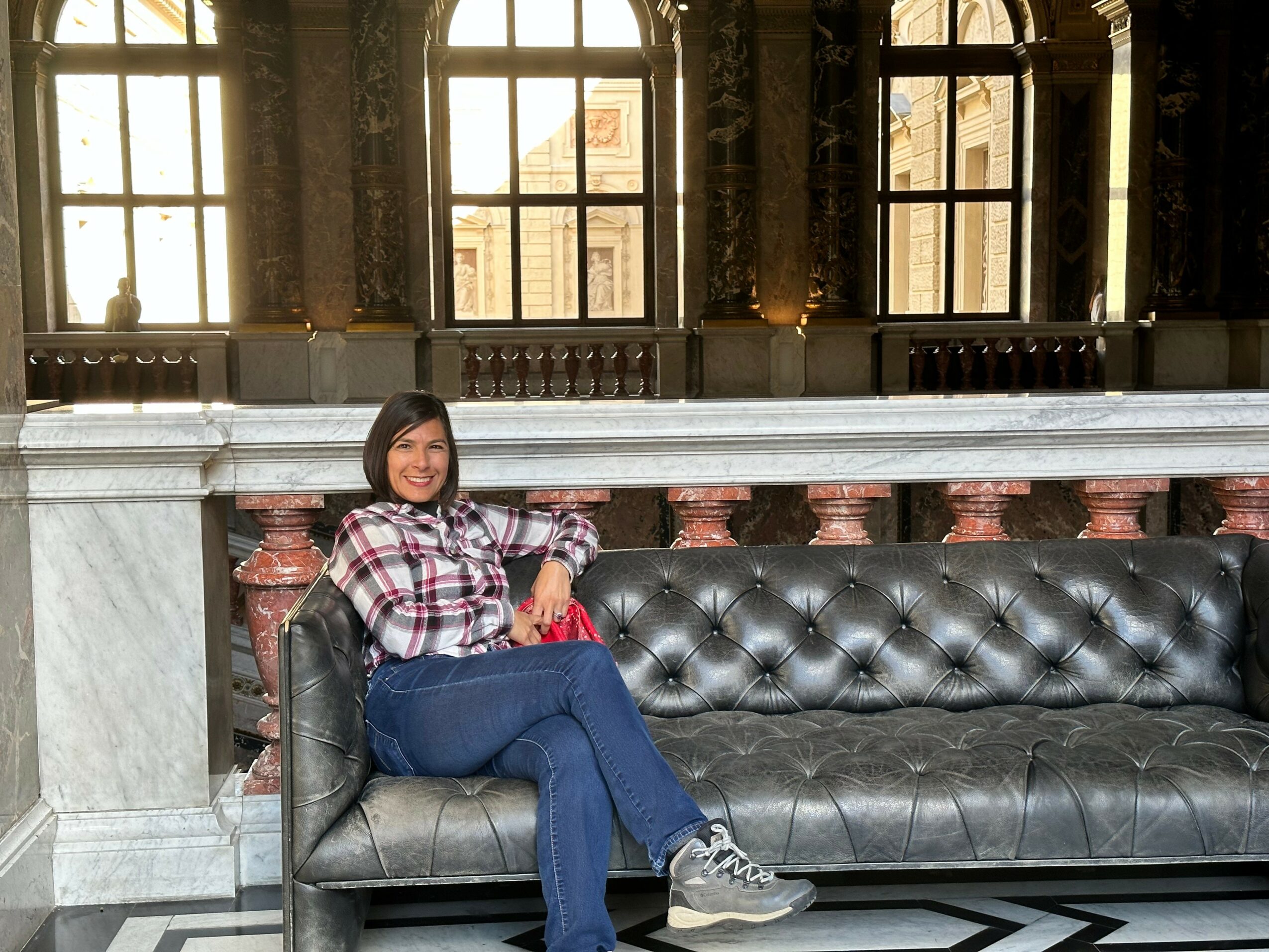 Woman sitting on a black leather sofa in a historic building with large windows and ornate interior.