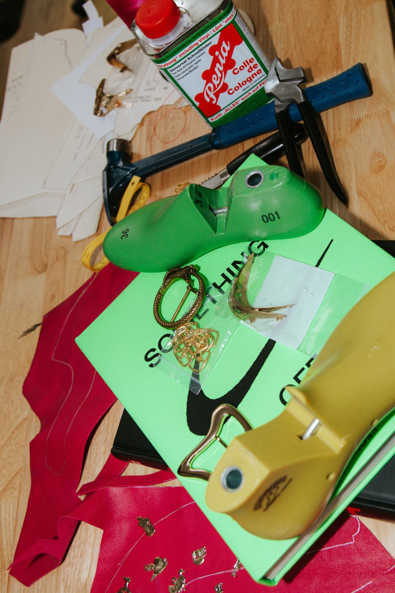 Green shoe, yellow shoe, scissors, and papers on a wooden surface with a glue bottle and other items.