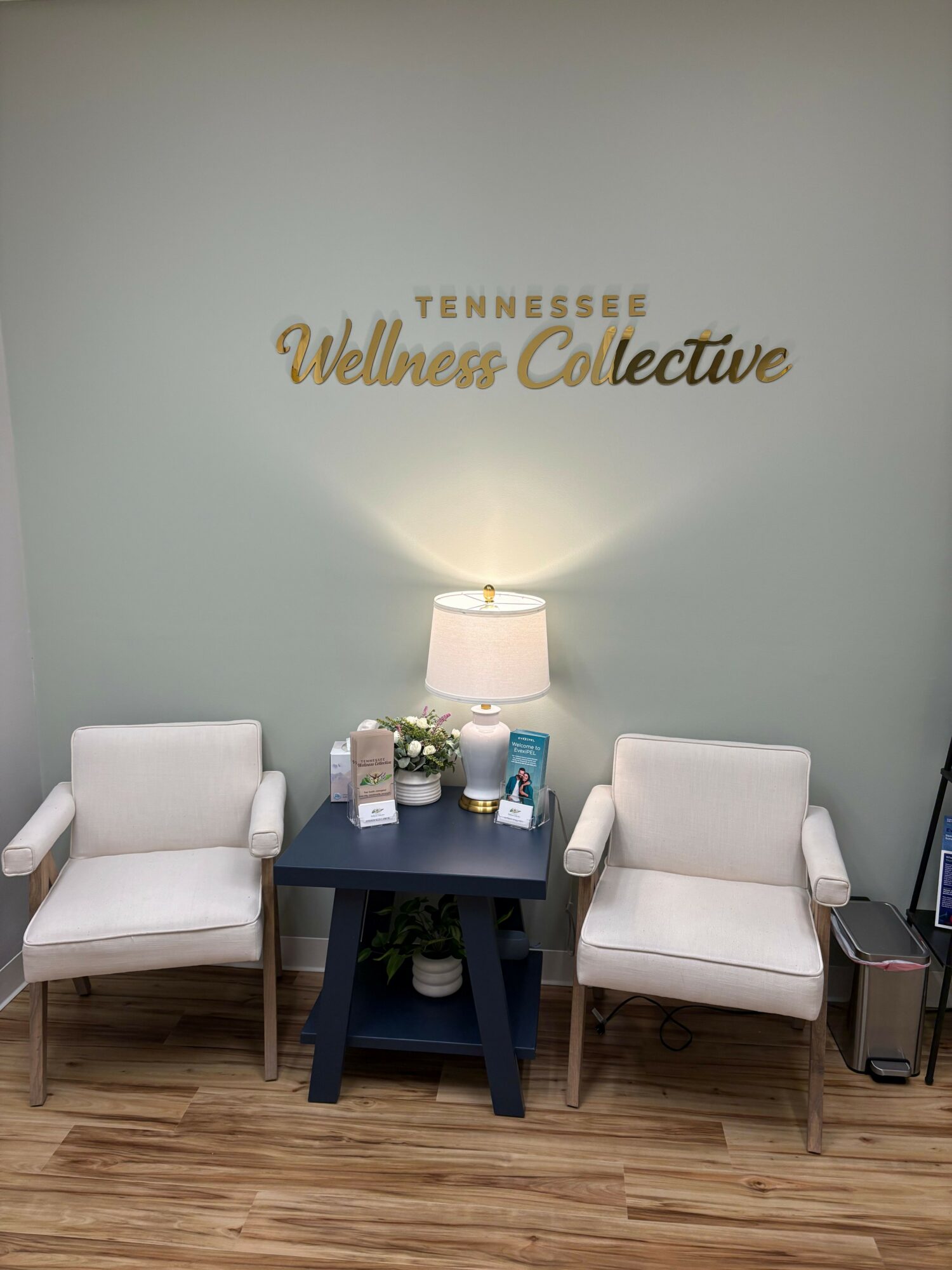 Waiting area with two white chairs, a blue table with a lamp, and decorative items against a wall with gold text.