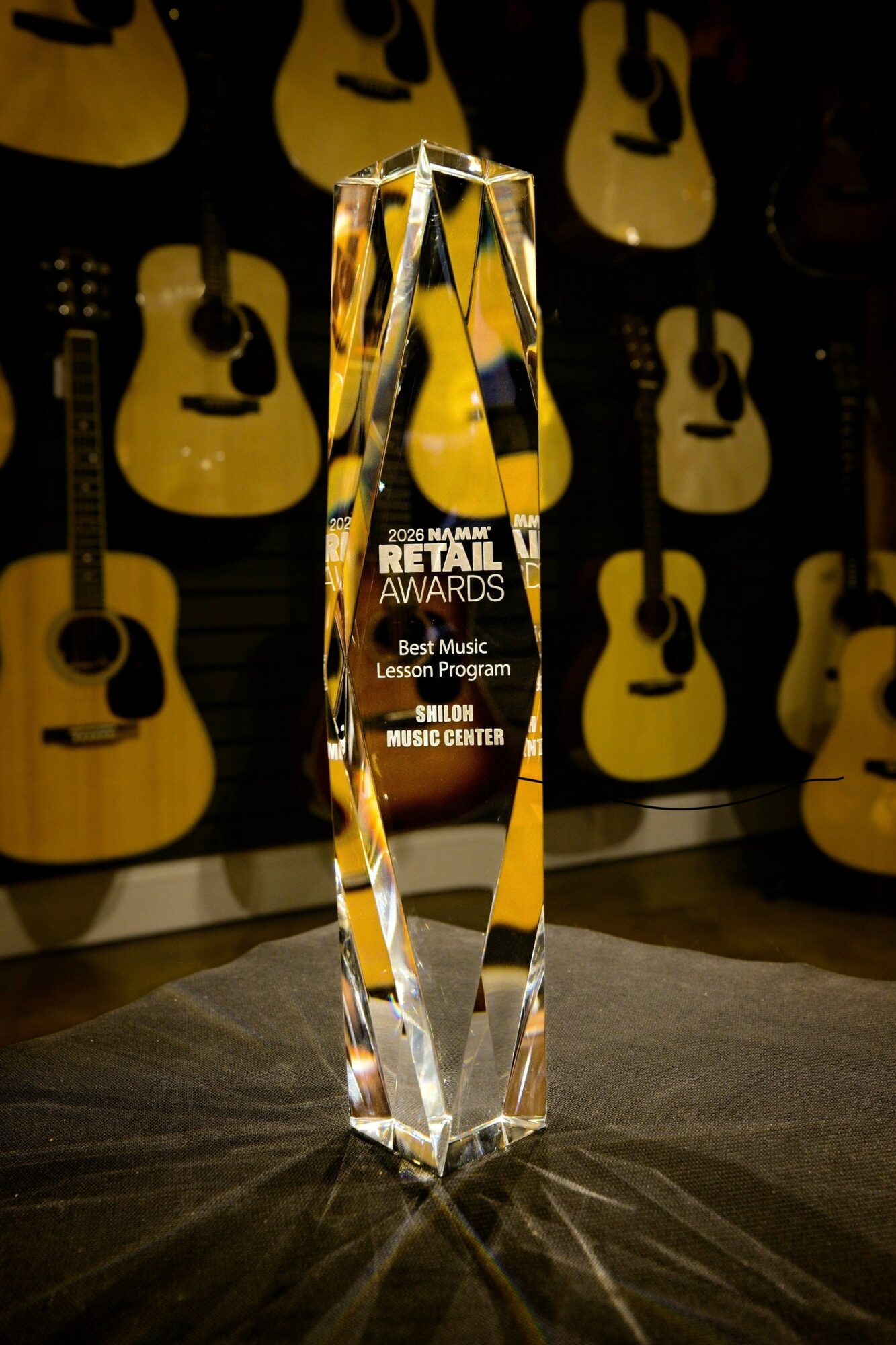 Crystal award with text for retail awards, set against a background of guitars, on a dark surface.
