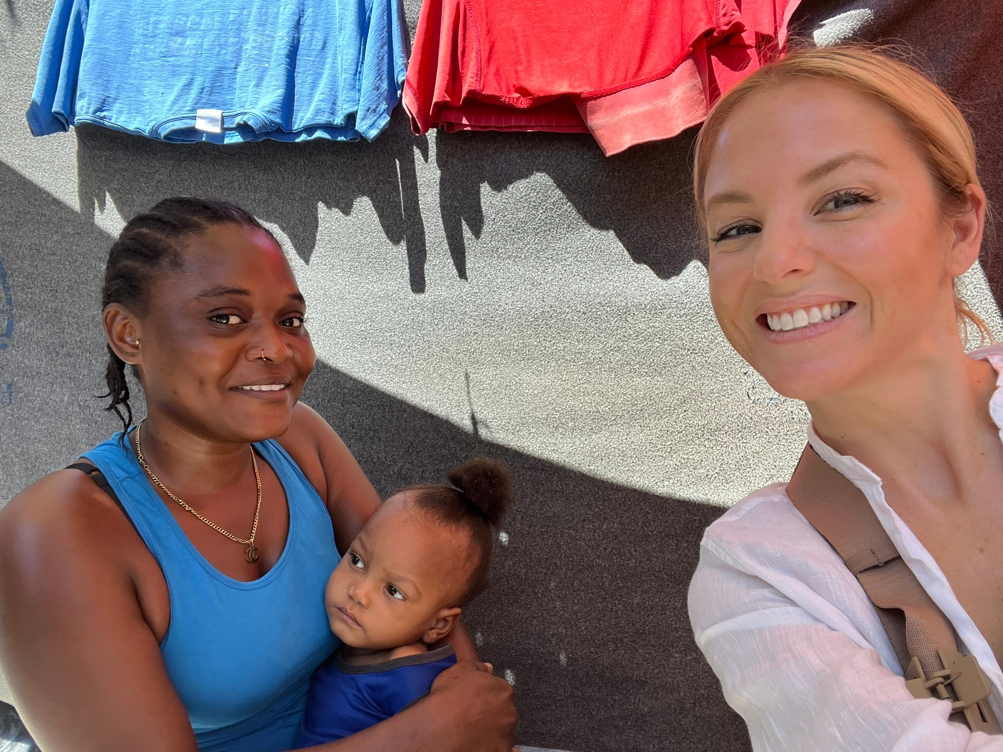 Two women and a child smiling, with colorful clothes hanging above them.