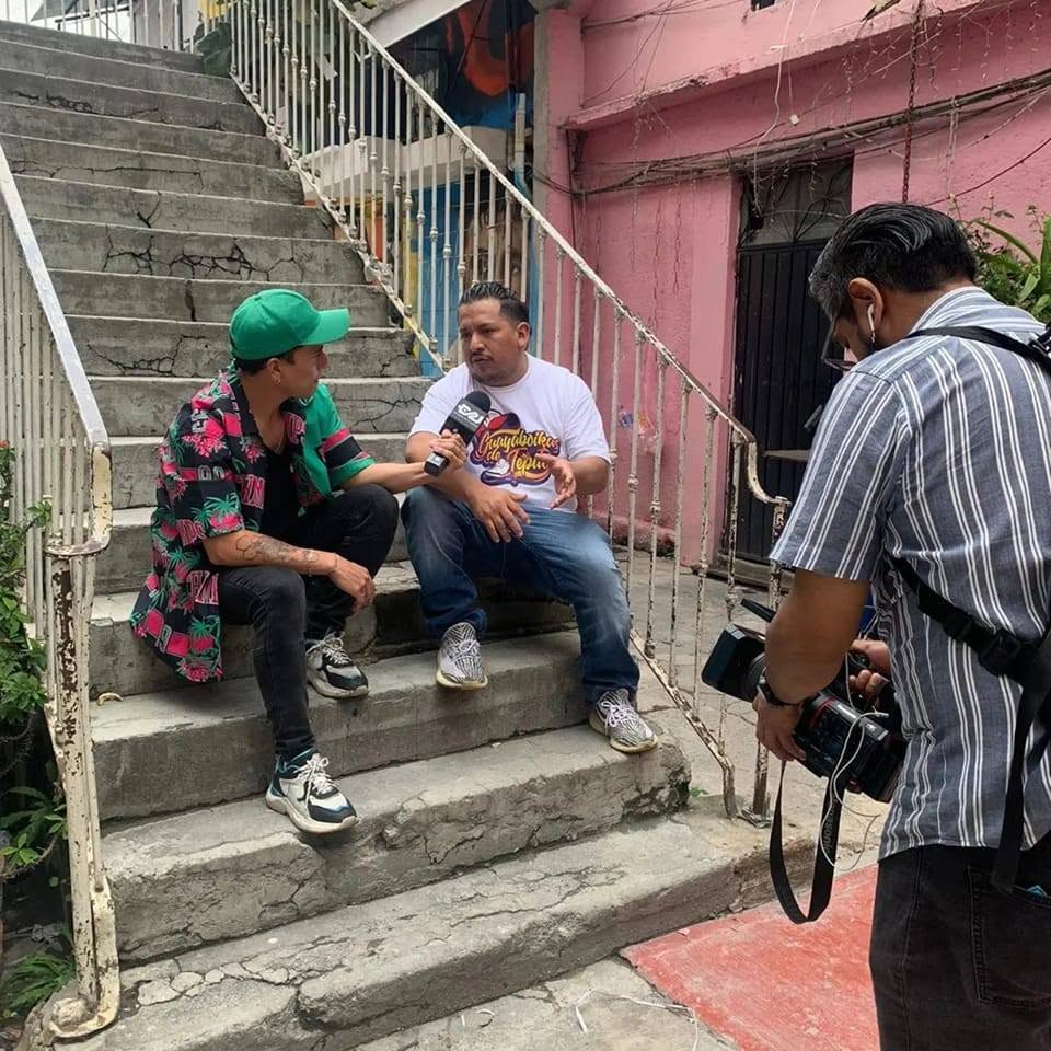 Two people sitting on stairs and talking, a photographer taking their picture, in an outdoor urban setting.