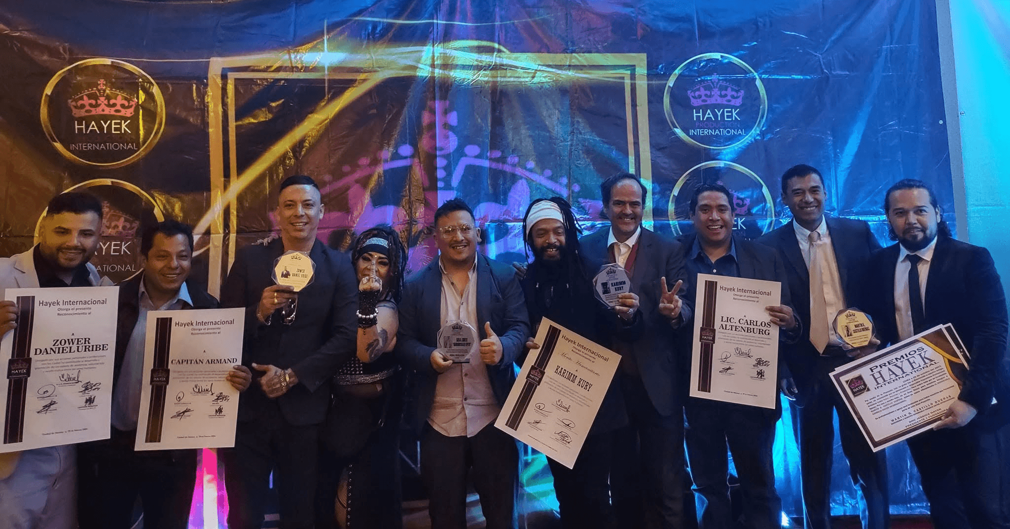 Group of people holding awards and certificates on stage with colorful lights and banners in the background.