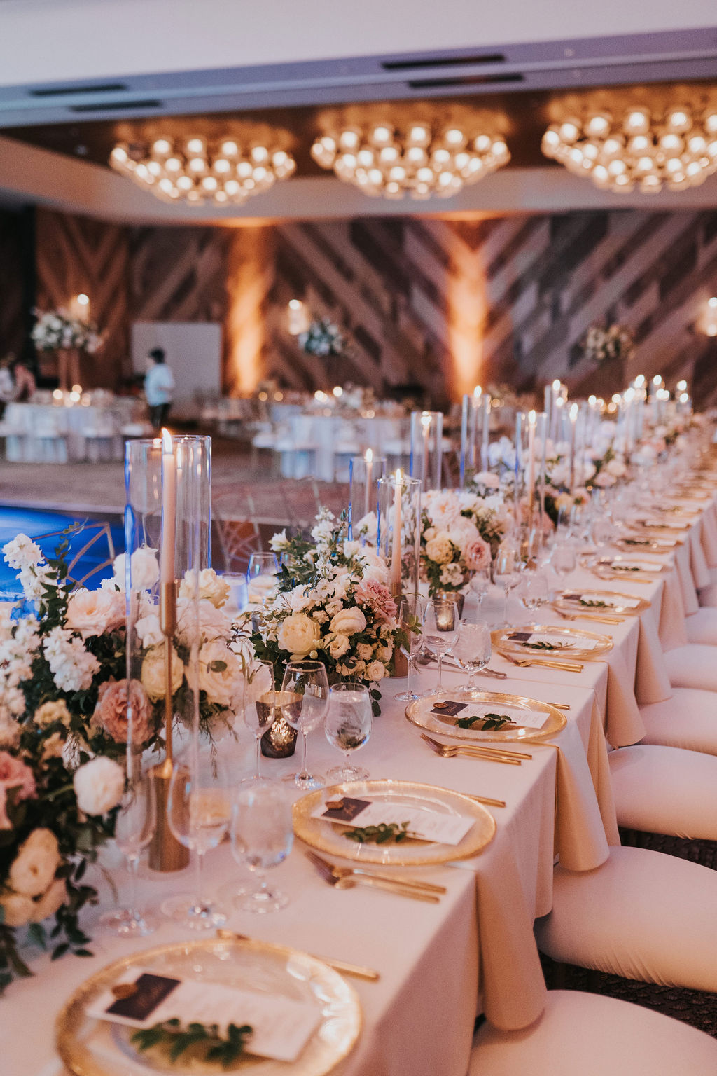 Elegant banquet table with floral arrangements, candles, and place settings in a decorated event hall.