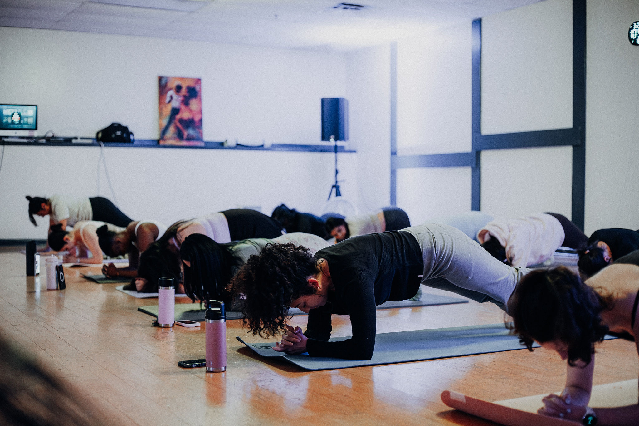 Group of people doing plank exercises on mats in a bright indoor space, with water bottles nearby.