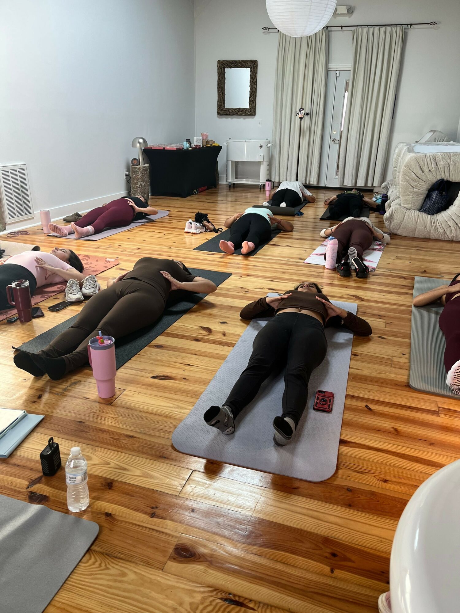 People practicing yoga on mats in a spacious room with wooden floors and white walls.