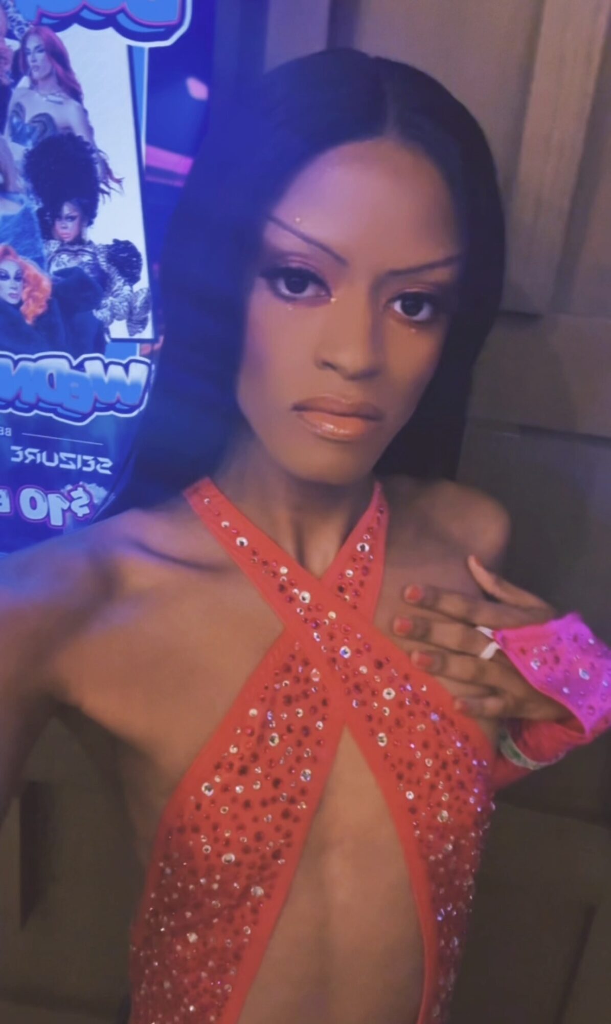 Woman with dark hair in a red, rhinestone-studded outfit, posing indoors with a serious expression.