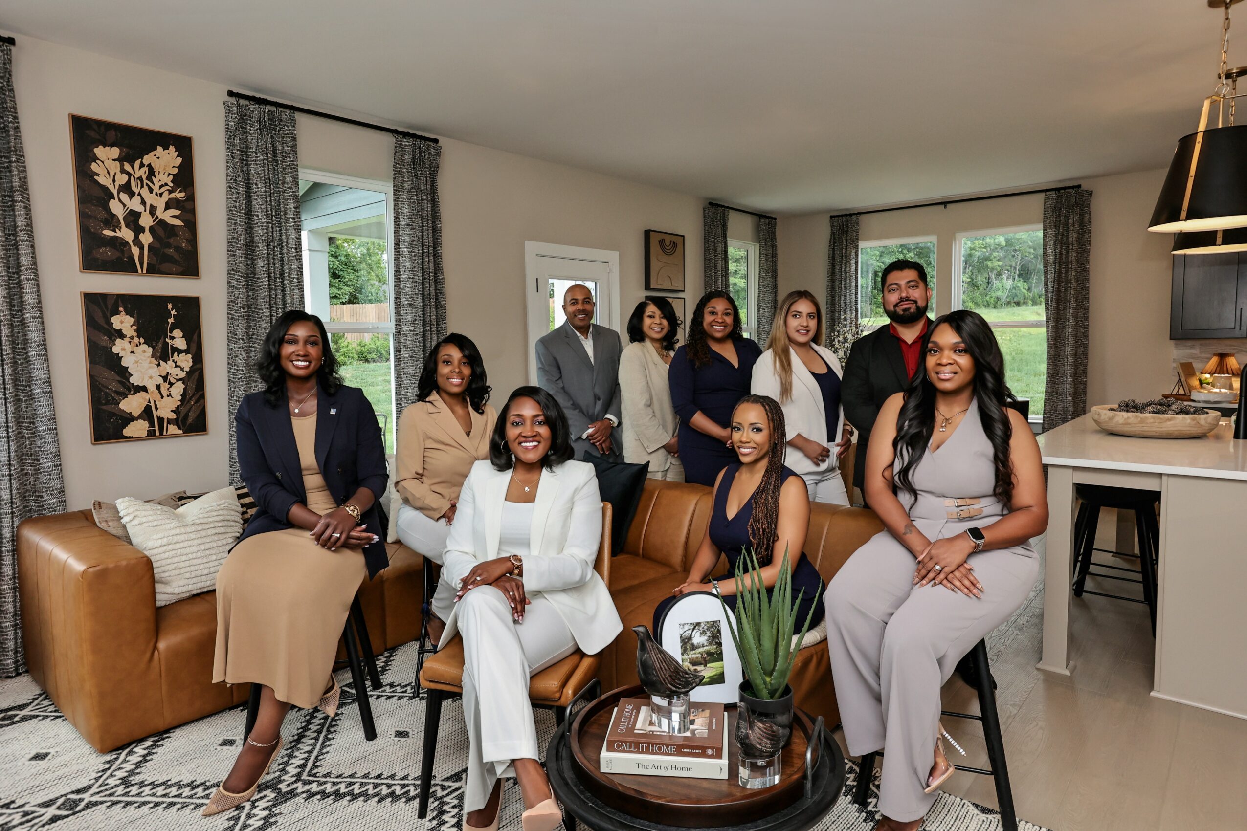 Group of ten diverse people gathered in a living room, smiling and posing for a photo, with furniture and artwork visible.