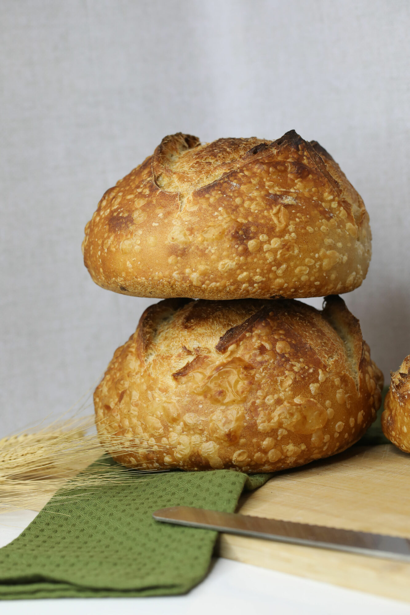 Two large, golden-brown fried pastries stacked on a wooden surface with a green cloth and a knife nearby.
