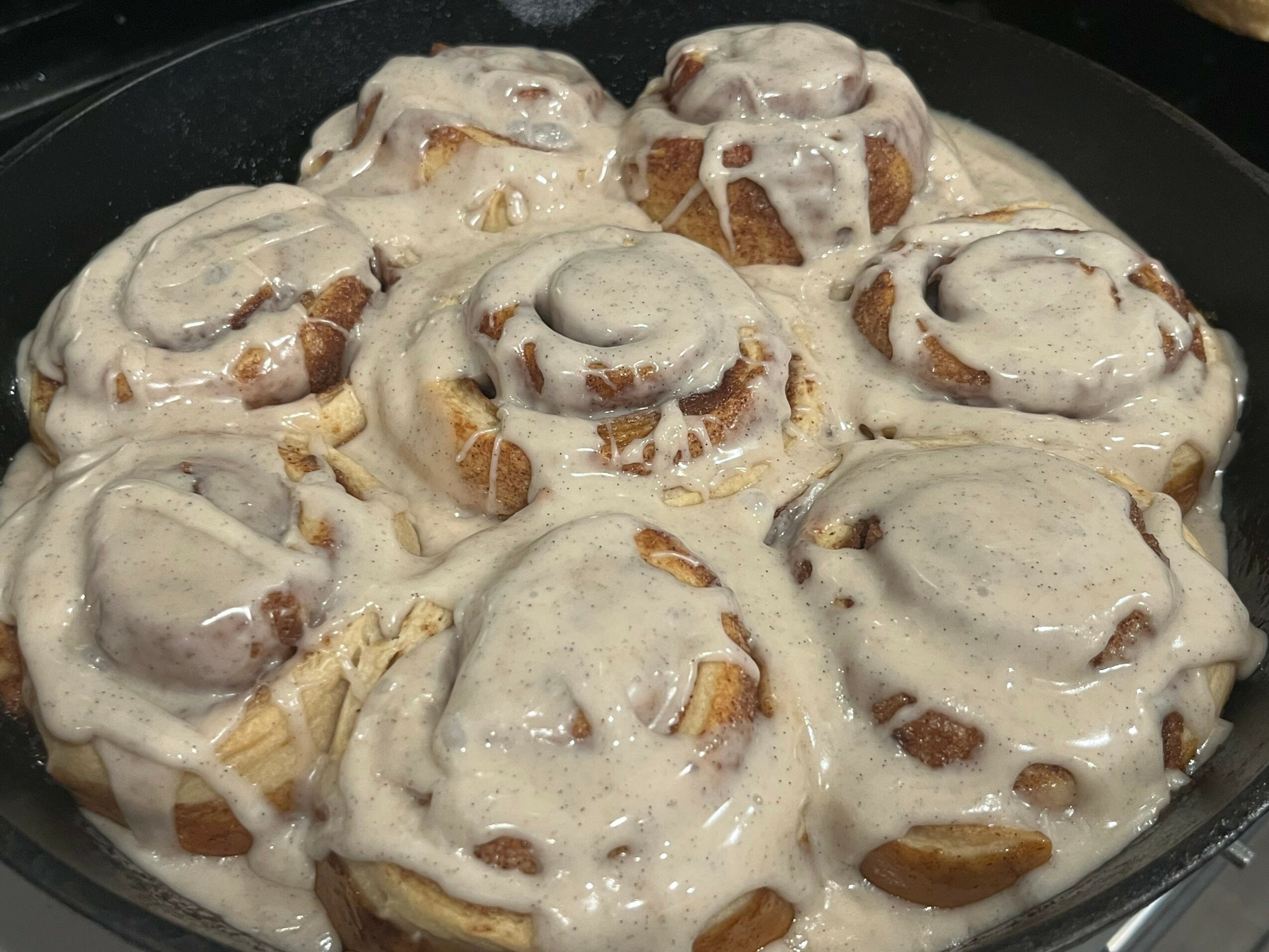 Cinnamon rolls with icing in a baking dish, topped with creamy glaze, arranged in a circular pattern.