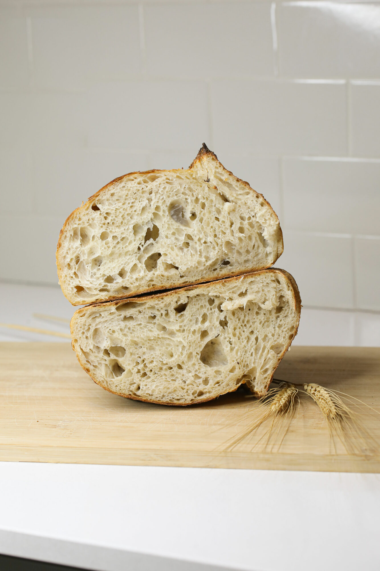 Two halves of a loaf of bread on a wooden surface, with a white tiled wall in the background.