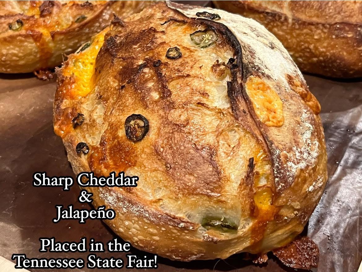 Close-up of a baked bread roll with cheese, jalapeño, and black olives, on a baking sheet.