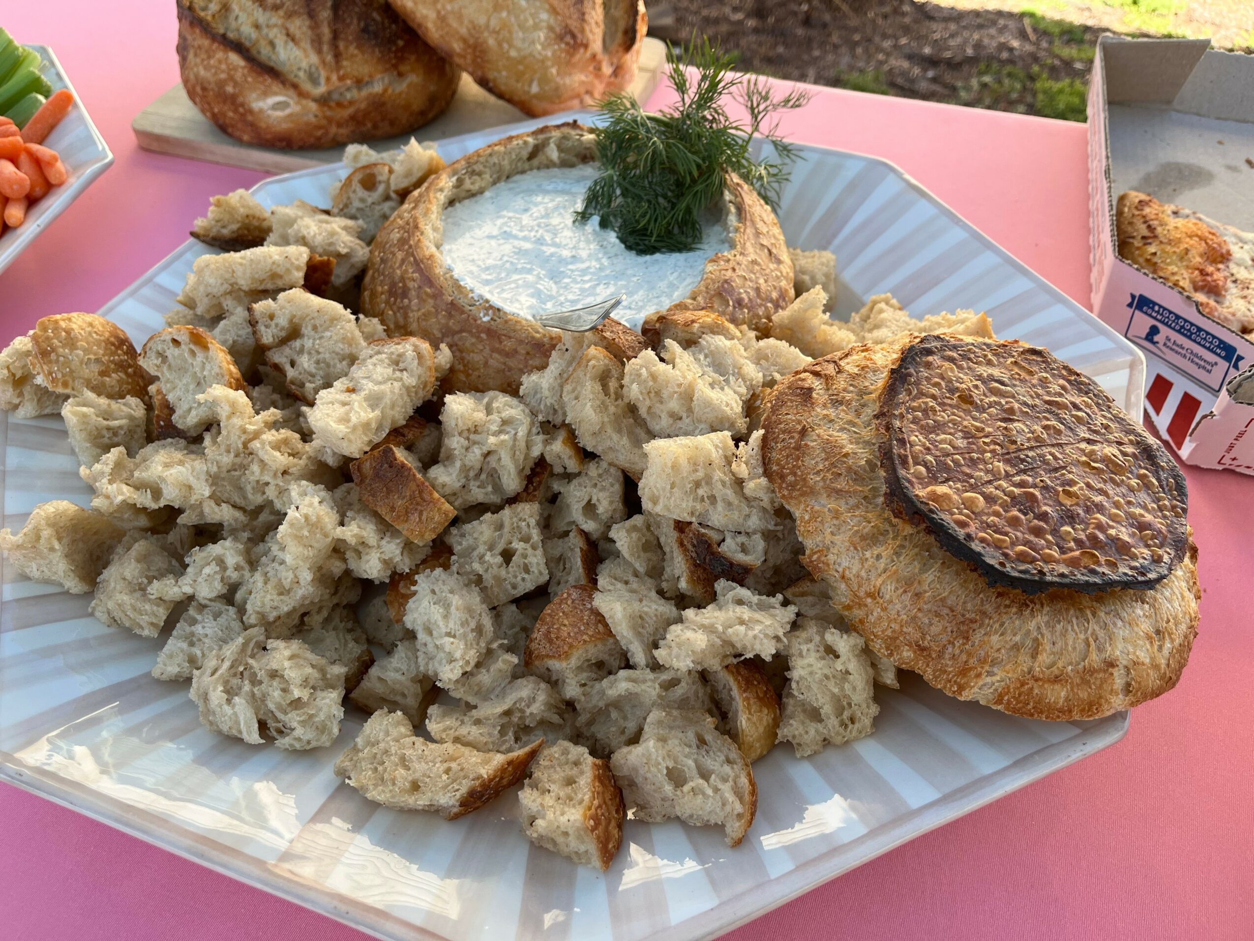 Plate with fried bread pieces, a bowl of creamy dip topped with herbs, and a fried patty on a pink surface.