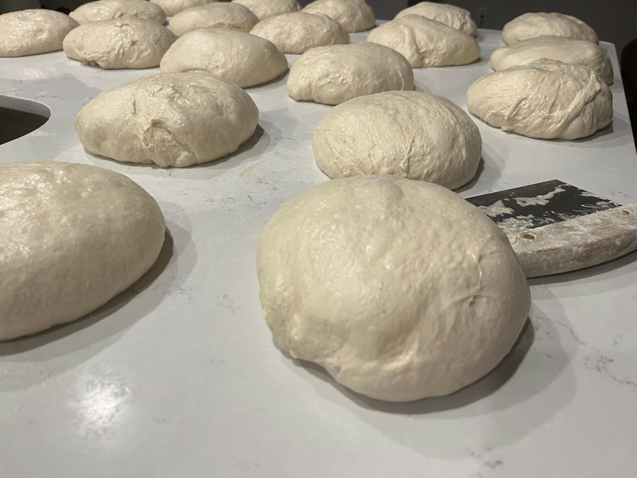 Several round dough balls on a white surface, some with a smooth surface, others slightly textured.