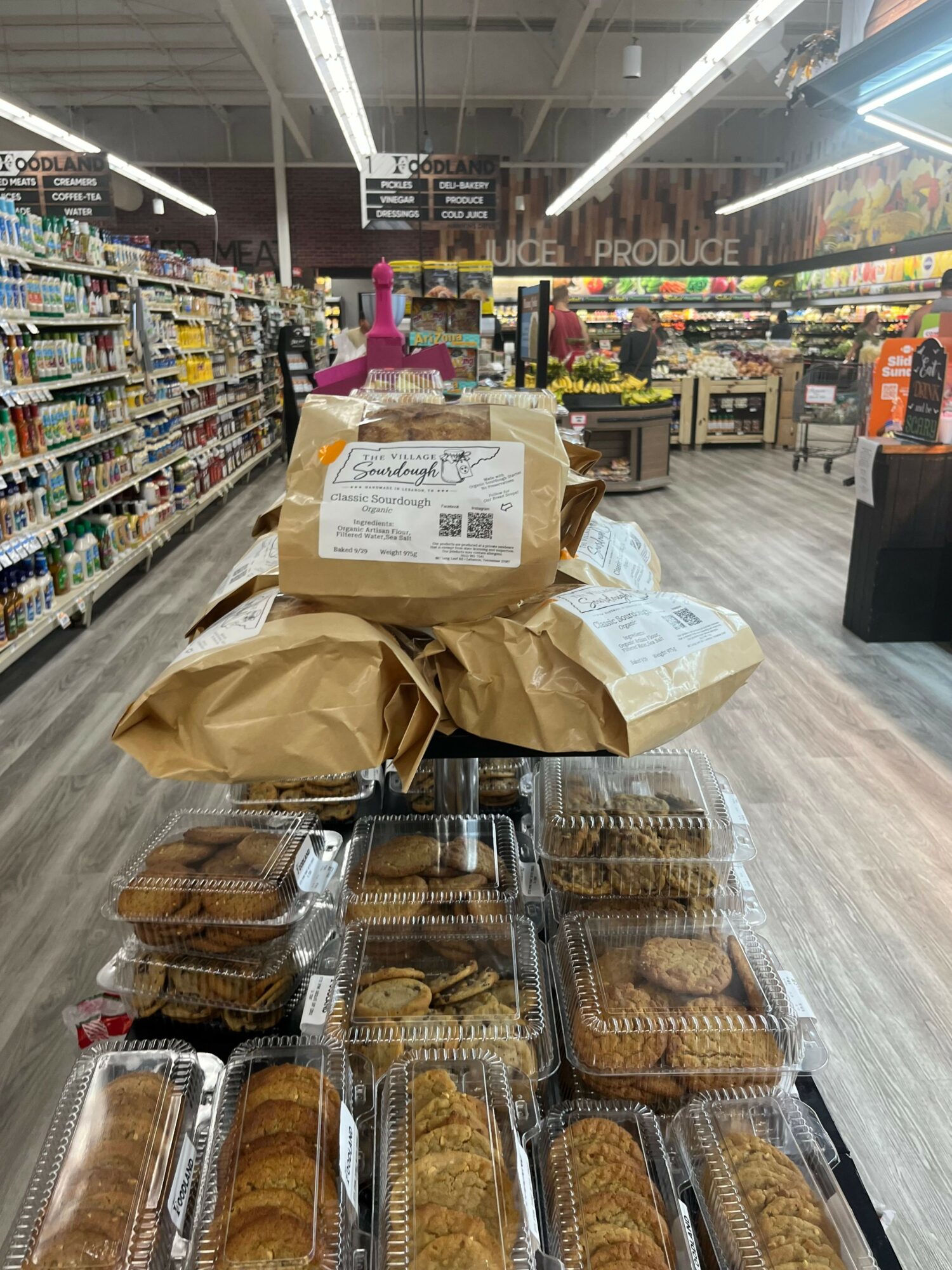 Bakery items in plastic containers and paper bags on a store counter, with shelves and products in the background.