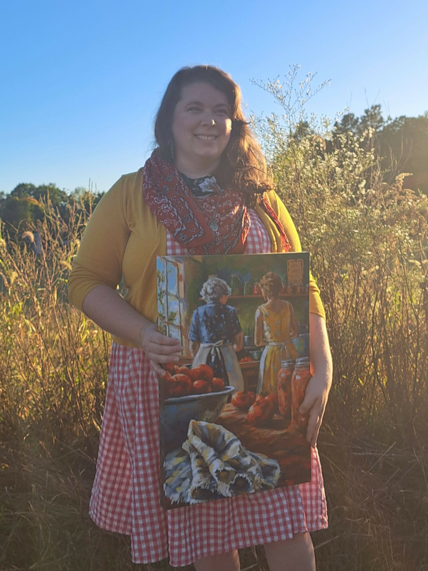 Woman holding a painting outdoors with trees and blue sky in the background.