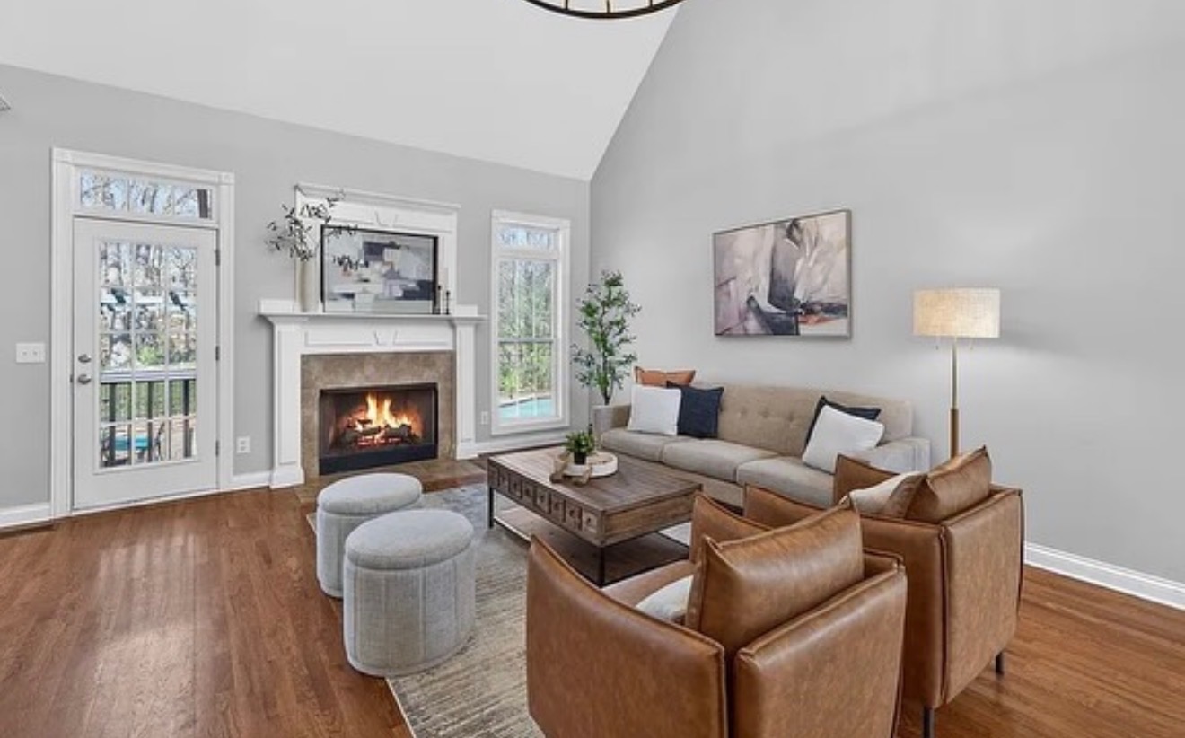 Living room with fireplace, sofa, armchairs, and large windows, decorated with artwork and a floor lamp.