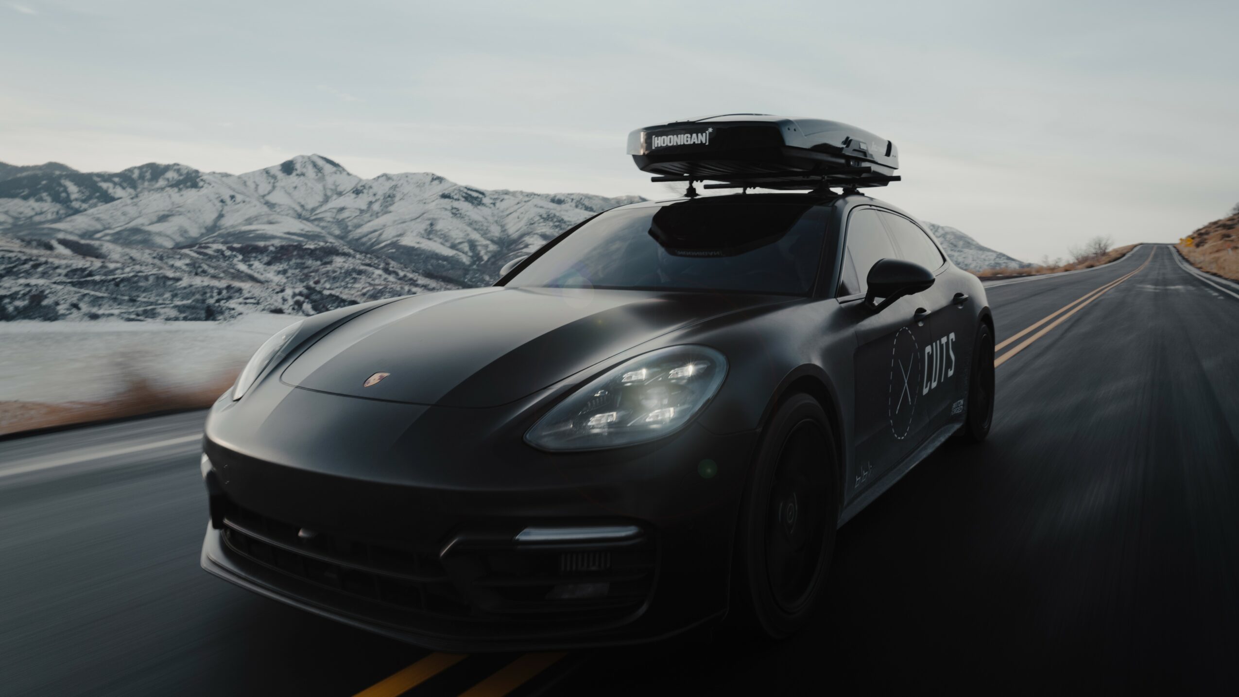 Black autonomous vehicle on a road with mountains in the background, a roof-mounted sensor system, and a license plate reading 'ATIS'.