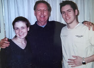 Three people standing together indoors, smiling, with a curtain background.
