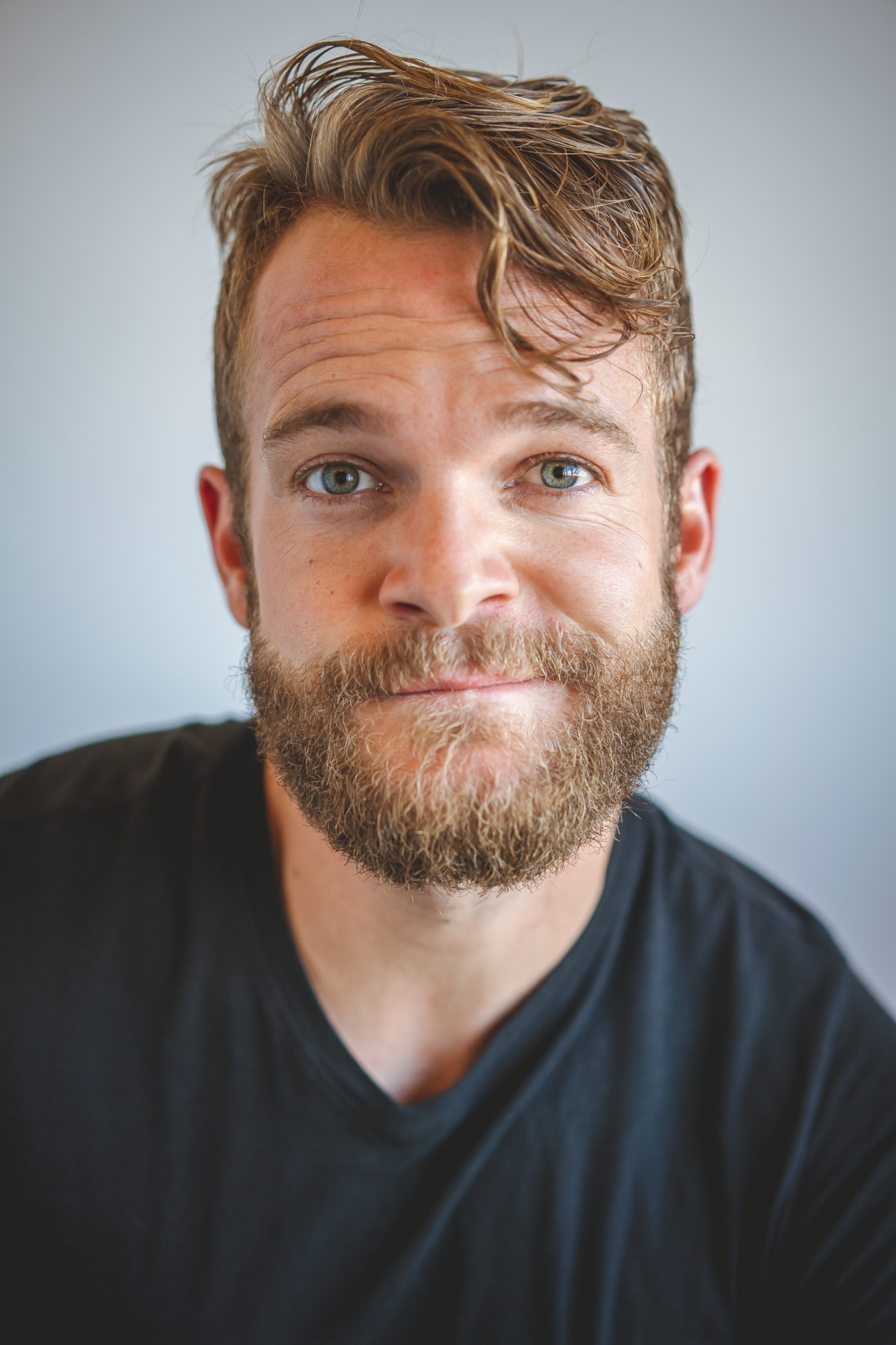 Portrait of a man with light brown hair, beard, and blue eyes, wearing a black shirt, smiling slightly.
