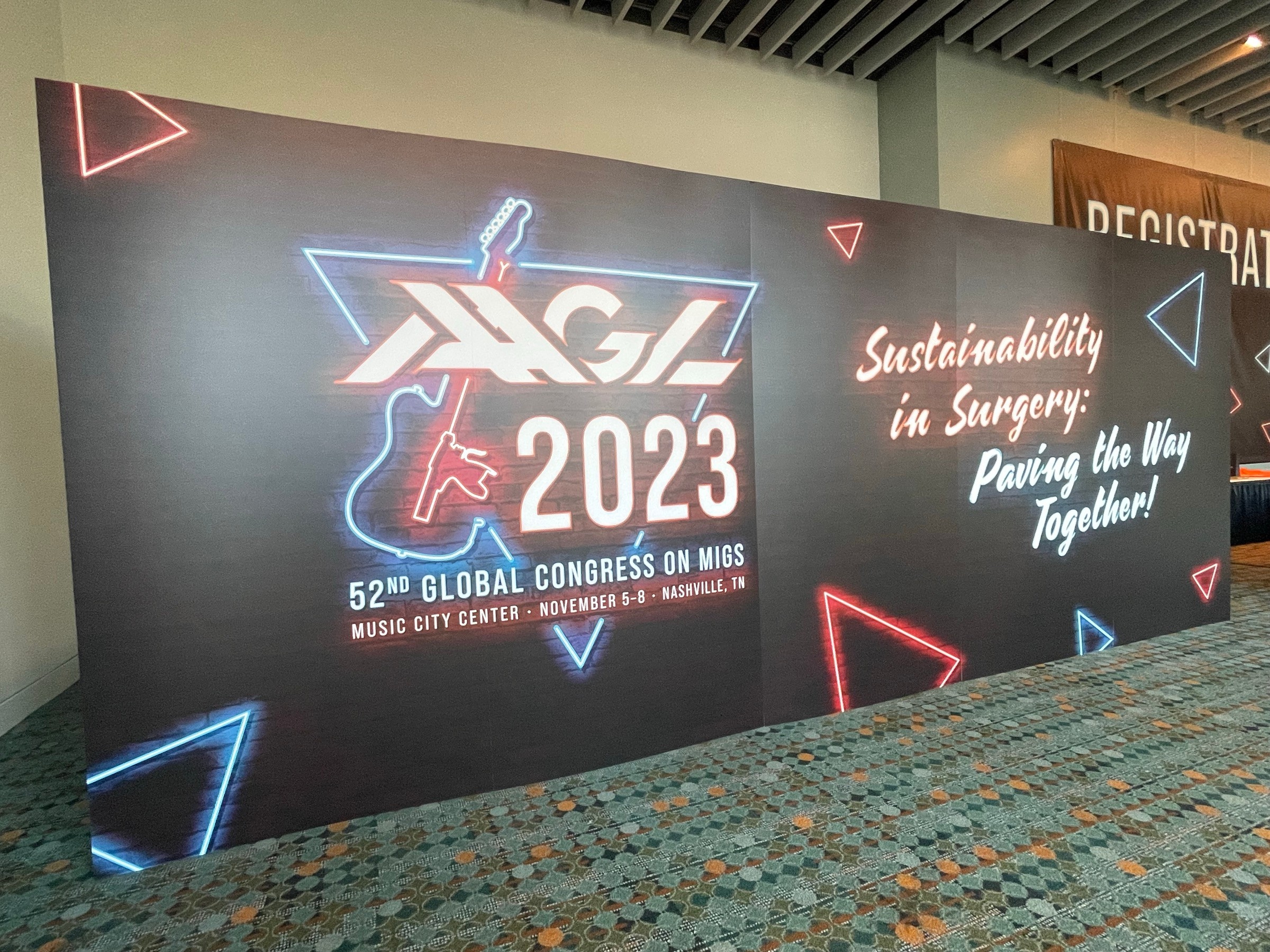 Large conference banner with logo, event details, and slogan about sustainability, colorful geometric shapes, and a patterned carpet.