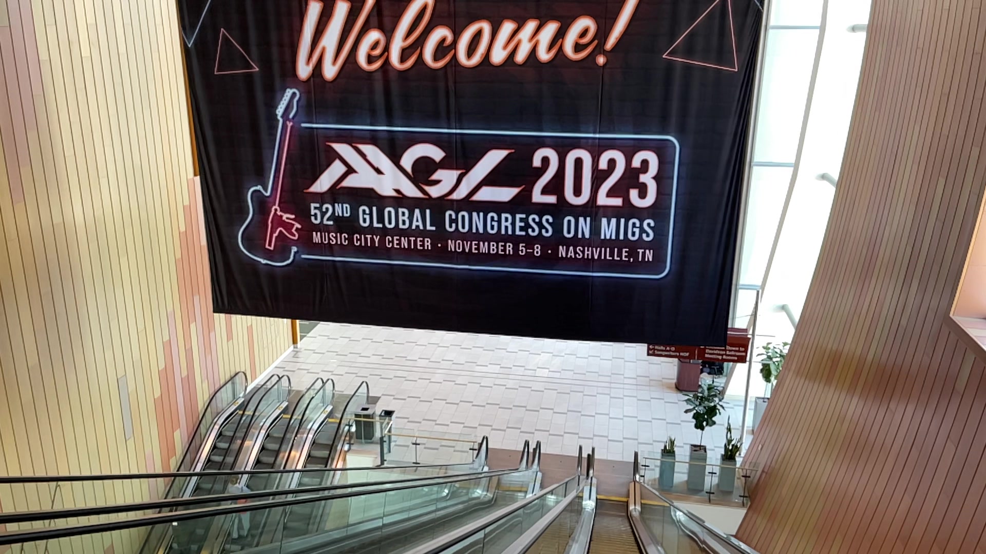 Escalator leading to a sign for the 2023 Global Congress on MIGs, with a welcome message and event details.