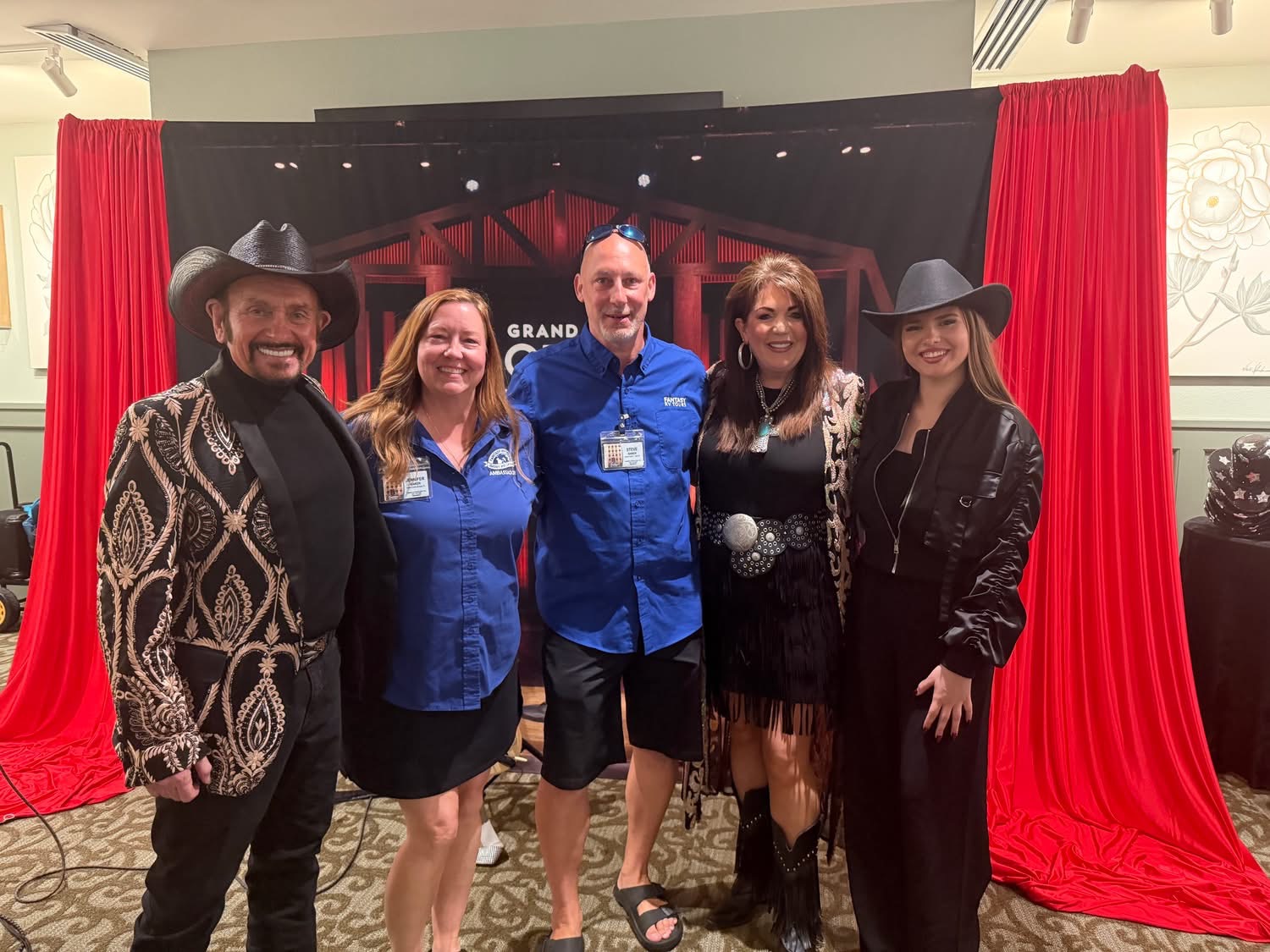 Five people standing in front of a red curtain and stage backdrop, smiling for the photo.