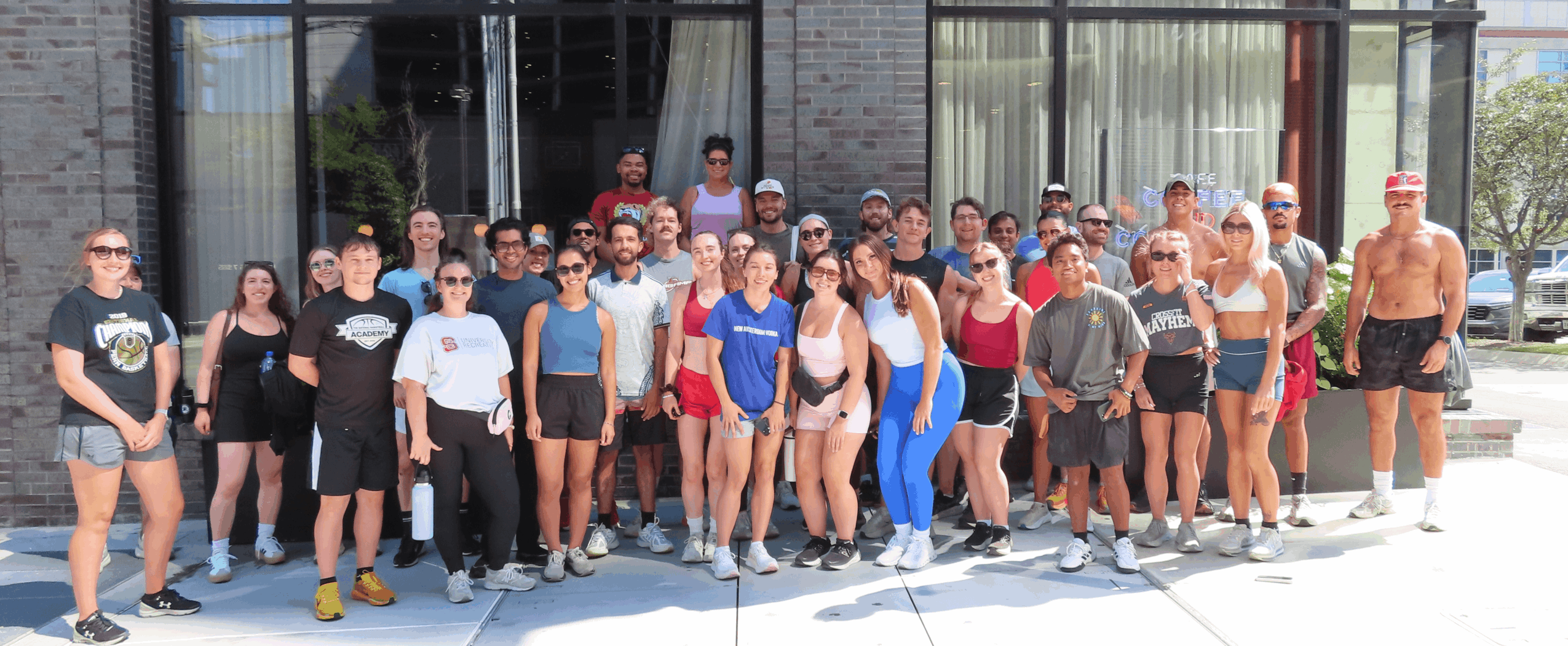 Group of people standing outside in front of a building, some wearing sunglasses and casual clothing.