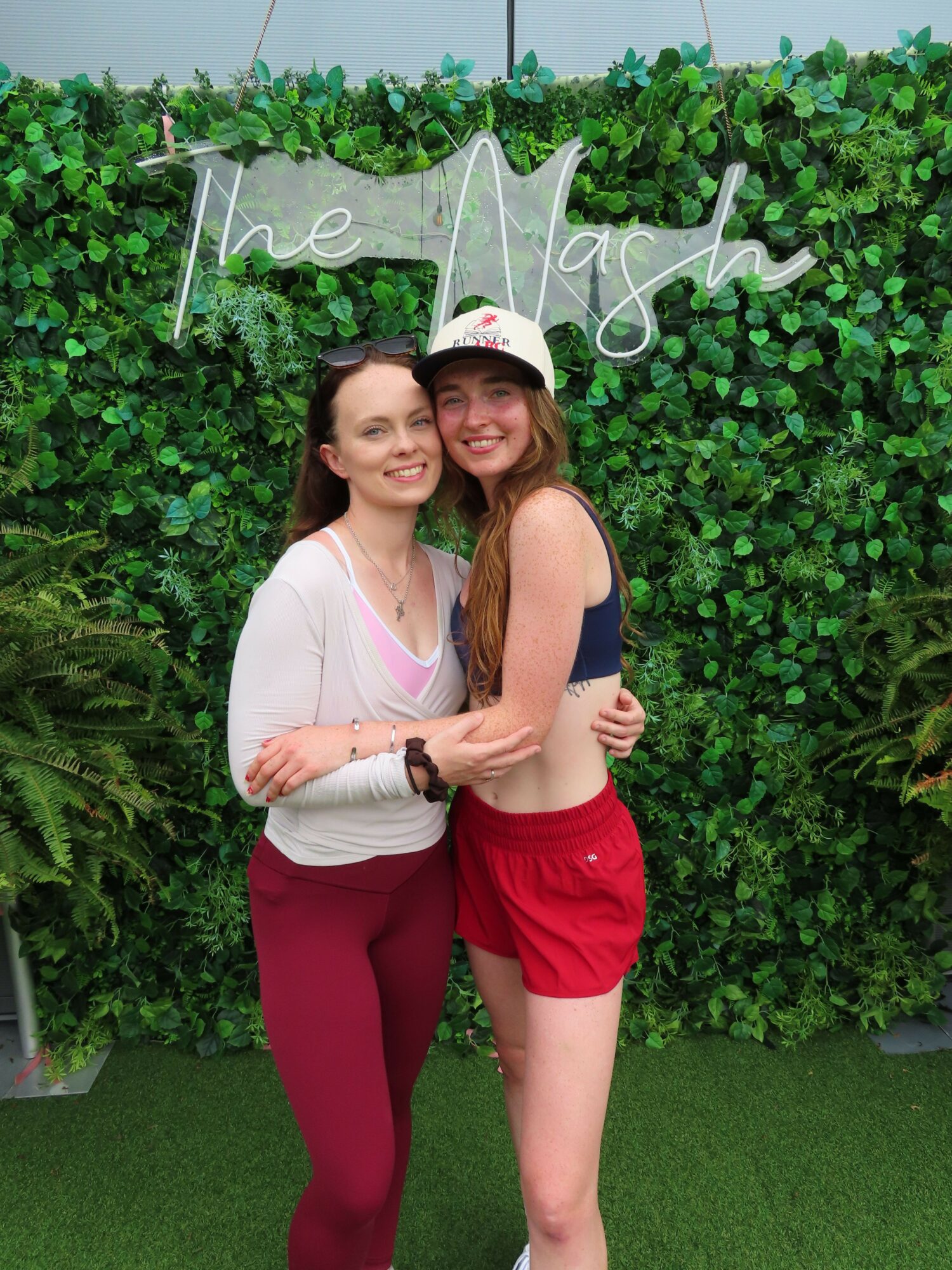 Two women hugging in front of green foliage and a decorative sign that says 'love' with a star shape.