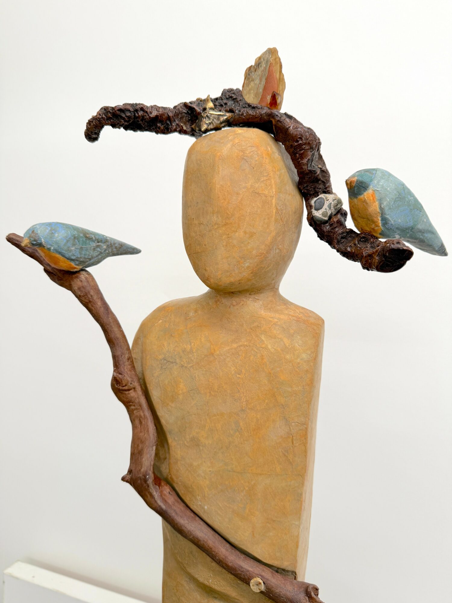 Sculpture of a headless figure with branches and birds attached, set against a plain white background.