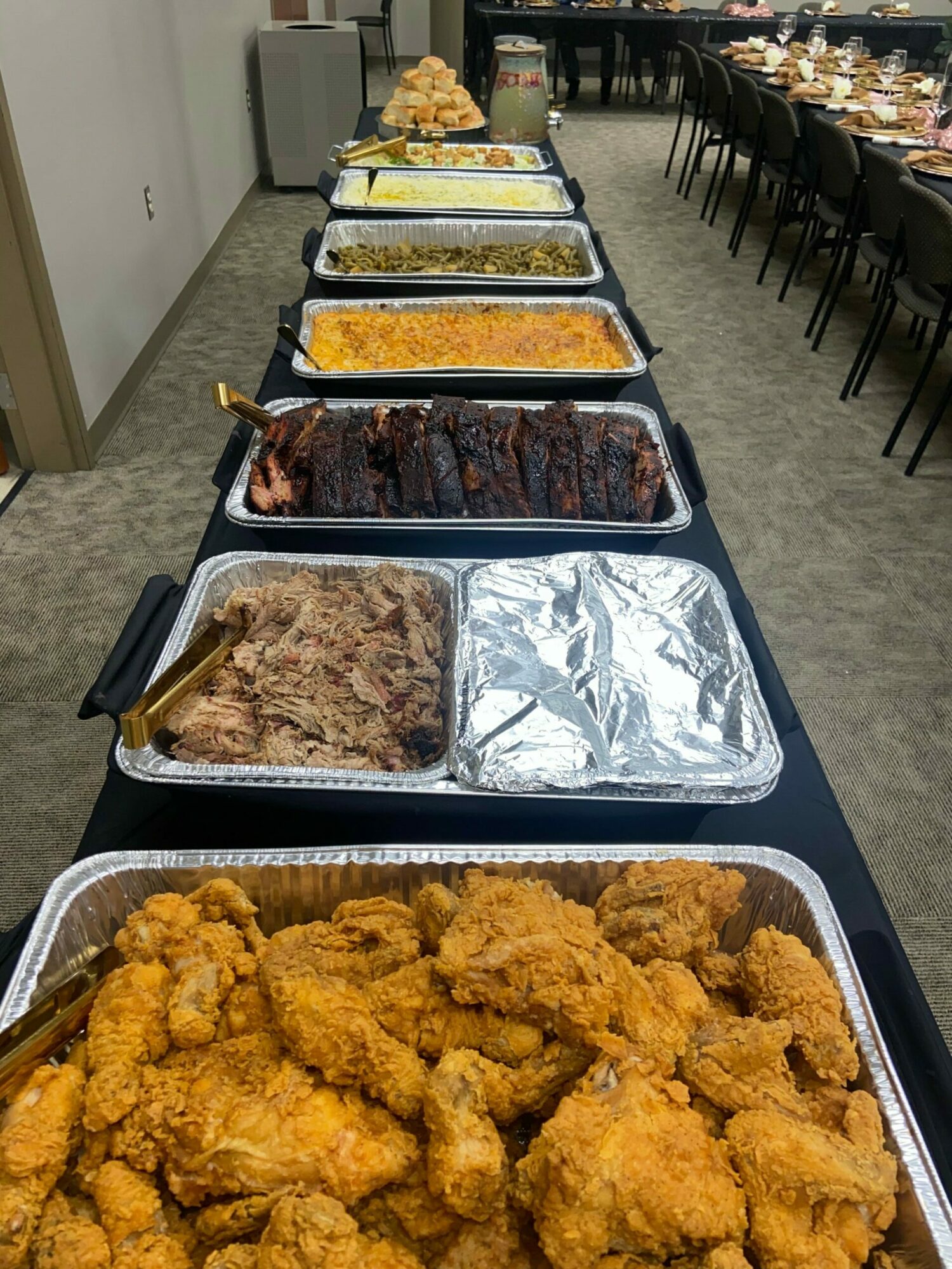 Tray of fried chicken pieces, several trays of cooked meat, rice, and other dishes on a table in a buffet setting.
