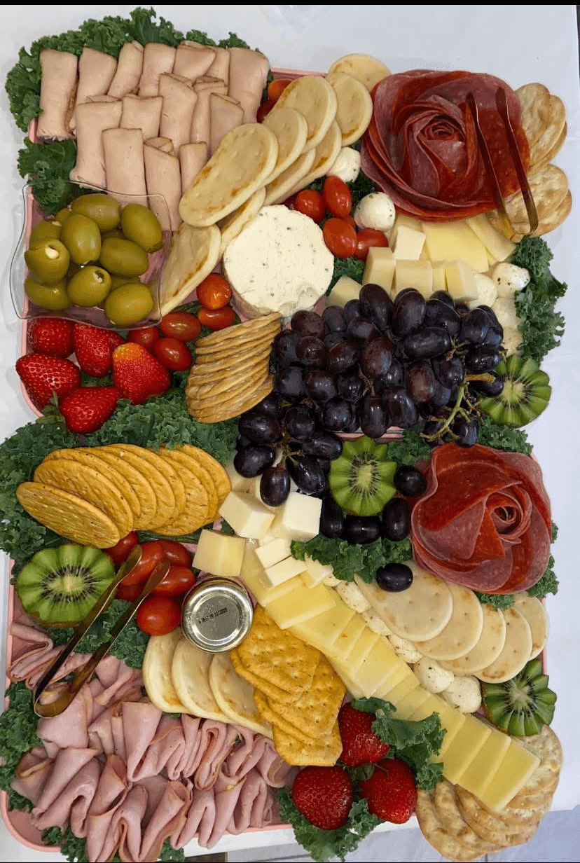 Assorted cheese, meats, grapes, strawberries, olives, and crackers arranged on a platter with garnishes.